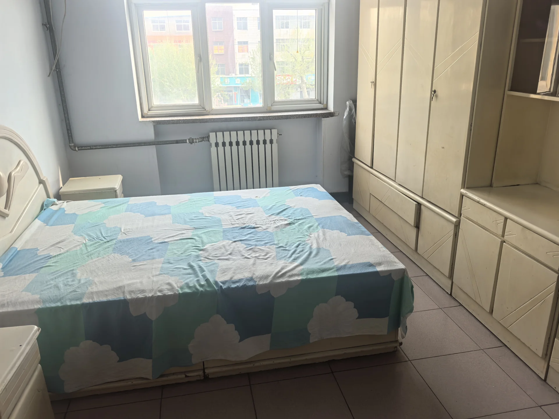 小卧室，整洁的双人床，自然光充足，温暖的暖气，宁静舒适的氛围。关键字:小卧室 双人床 自然光 暖气 宁静舒适