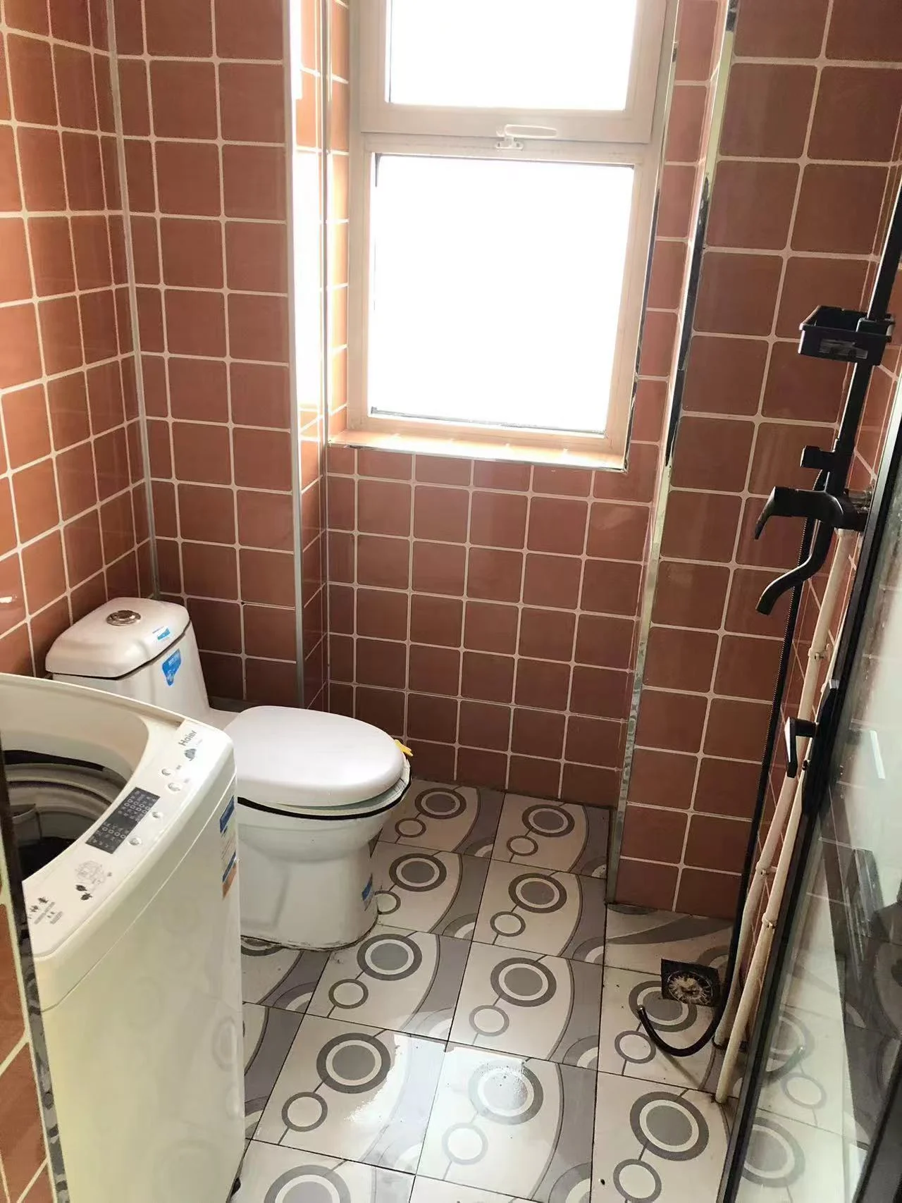 小而整洁的卫生间，白色瓷砖地面和墙面。马桶位于房间中央，洗衣机靠墙放置。两个洗手盆分别靠近左墙和后方。窗户带来自然光，整体氛围宁静整洁，设计简约注重实用性。关键字:小卫生间 白色瓷砖 马桶 洗衣机 两个洗手盆 自然光 宁静整洁 简约设计