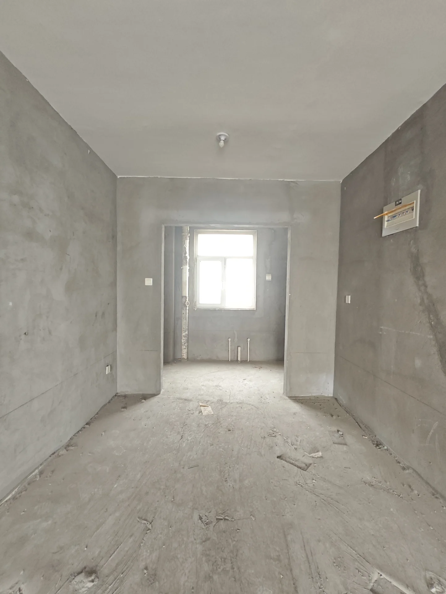 房间以水泥墙和地板为主，显得正在施工中。窗户提供自然光，但墙面裸露未完工，空间显得空旷无人。混凝土天花板增添了工业感。整体氛围宁静而简约，没有活动迹象。关键字:水泥墙 地板 施工中 自然光 裸露墙面 工业感 宁静氛围
