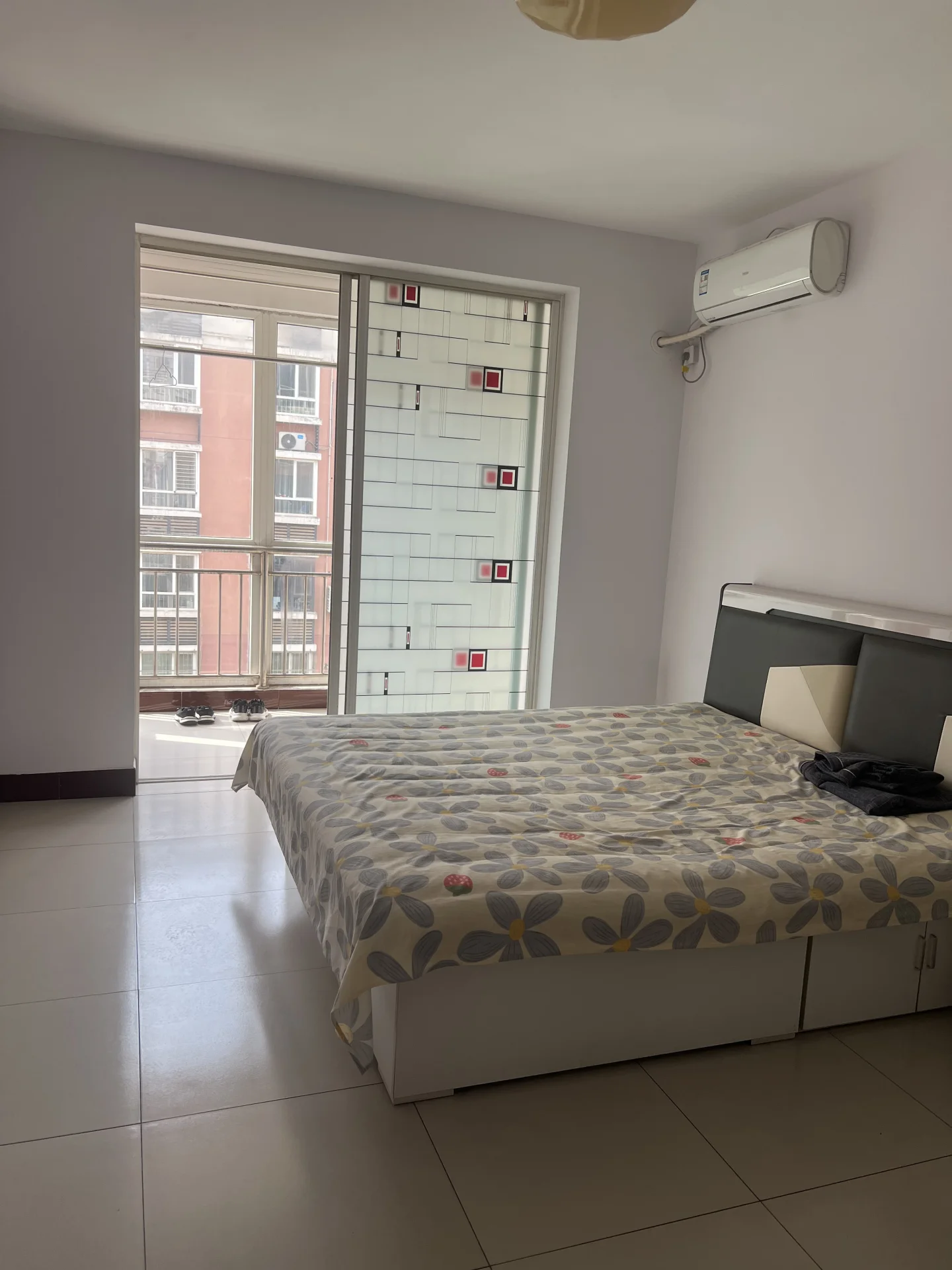 温馨的小卧室，白墙白地，整洁干净。床居中摆放，窗边自然采光。墙上两个空调，靠右有一把椅子。整体氛围宁静宜人，适合放松或休息。关键字:小卧室 白墙 整洁 自然采光 空调 椅子 宁静氛围