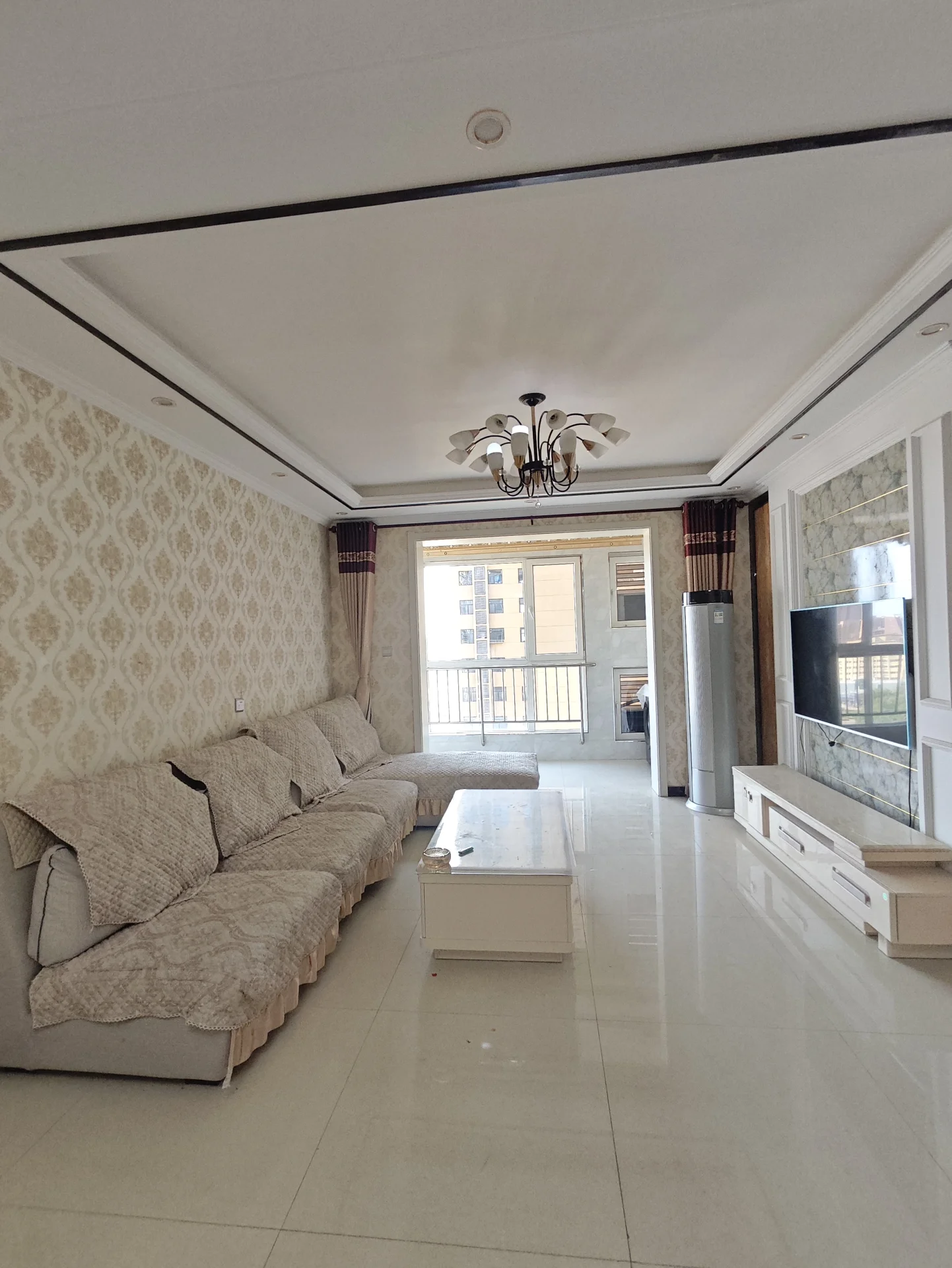 宽敞明亮的客厅，白色墙面，两沙发布局合理，电视墙挂置，中央有餐椅，两侧窗户采光良好，窗边有绿植点缀。关键字:宽敞 明亮 白色墙面 沙发 电视墙挂置 餐椅 窗户采光 绿植