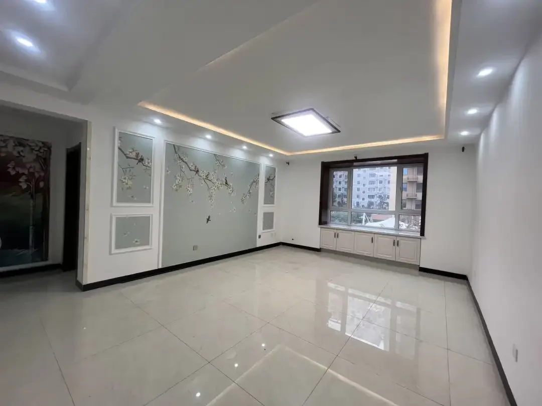 宽敞明亮的厨房或餐厅，白色墙壁，两侧各有窗户，左侧有门，中央放置冰箱，周围有多个橱柜和抽屉提供储物空间。关键字:大房间 白色墙壁 窗户 门 厨房 餐厅 冰箱 橱柜 抽屉