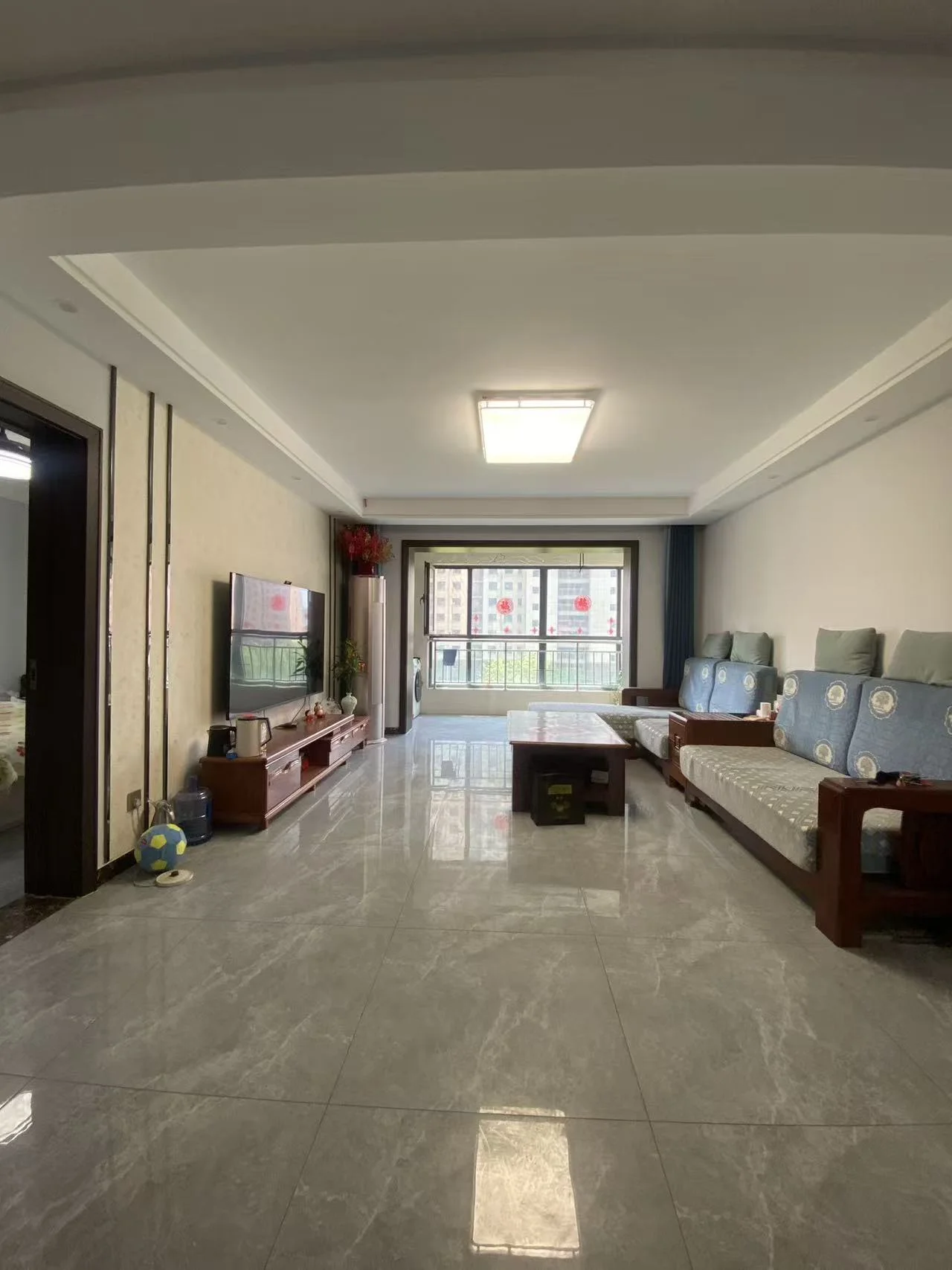 宽敞明亮的客厅，硬木地板，大窗户引入自然光，营造温馨氛围。电视、书籍、沙发、椅子和绿植点缀其间。关键字:客厅 硬木地板 自然光 电视 书籍 沙发 椅子 绿植