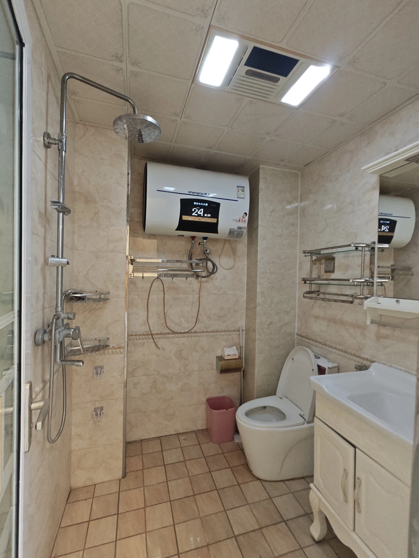 小而干净的卫生间，白墙瓷砖，配有马桶、洗手盆、淋浴和镜子。两座马桶，其中一座有粉色盖子。马桶上方有电子卷纸机。整体井然有序，充满宁静感。关键字:小卫生间 白墙瓷砖 马桶 洗手盆 淋浴 镜子 粉色盖子 电子卷纸机