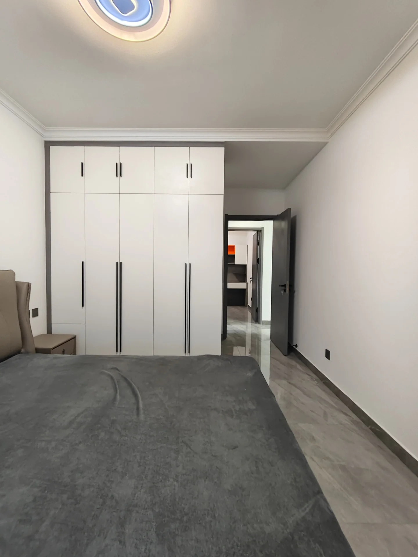 宽敞明亮的现代客厅，白色墙面，中央摆放着一张看似未整理的床。一侧有沙发，后墙附近也有另一张沙发。房间内还有椅子。空间显得空旷宁静，充满自然光。关键字:宽敞 明亮 现代 白色墙面 未整理的床 沙发 椅子 空旷宁静