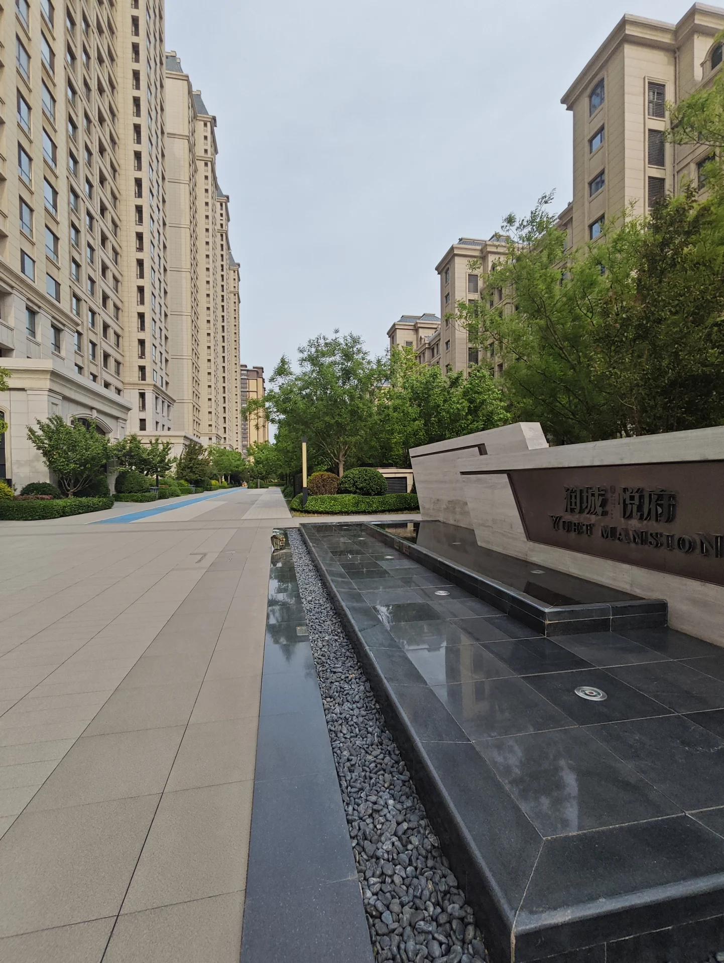 城市街道中央有一座大石 fountain，两侧是现代建筑。四周摆放着长椅，提供休息空间。一盆植物增添绿意，营造宁静氛围。城市背景中，大石结构与现代建筑形成鲜明对比。关键字:城市街道 大石 fountain 现代建筑 长椅 植物 宁静氛围