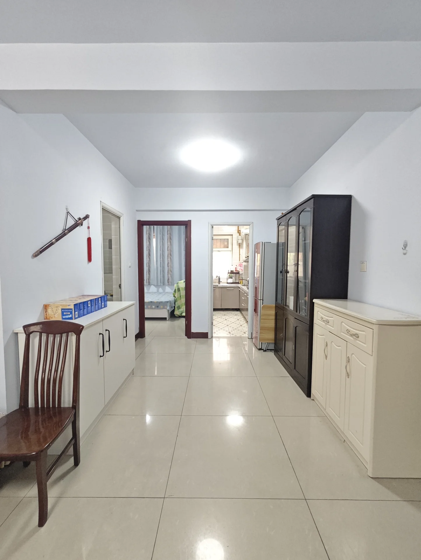 厨房整洁明亮，白色墙面和瓷砖地面，大窗户采光充足。相邻的客厅有沙发和椅子，整体氛围宁静宜人，现代简约风格。关键字:厨房 白色墙面 瓷砖地面 大窗户 自然光 客厅 沙发 椅子 整洁明亮 现代简约