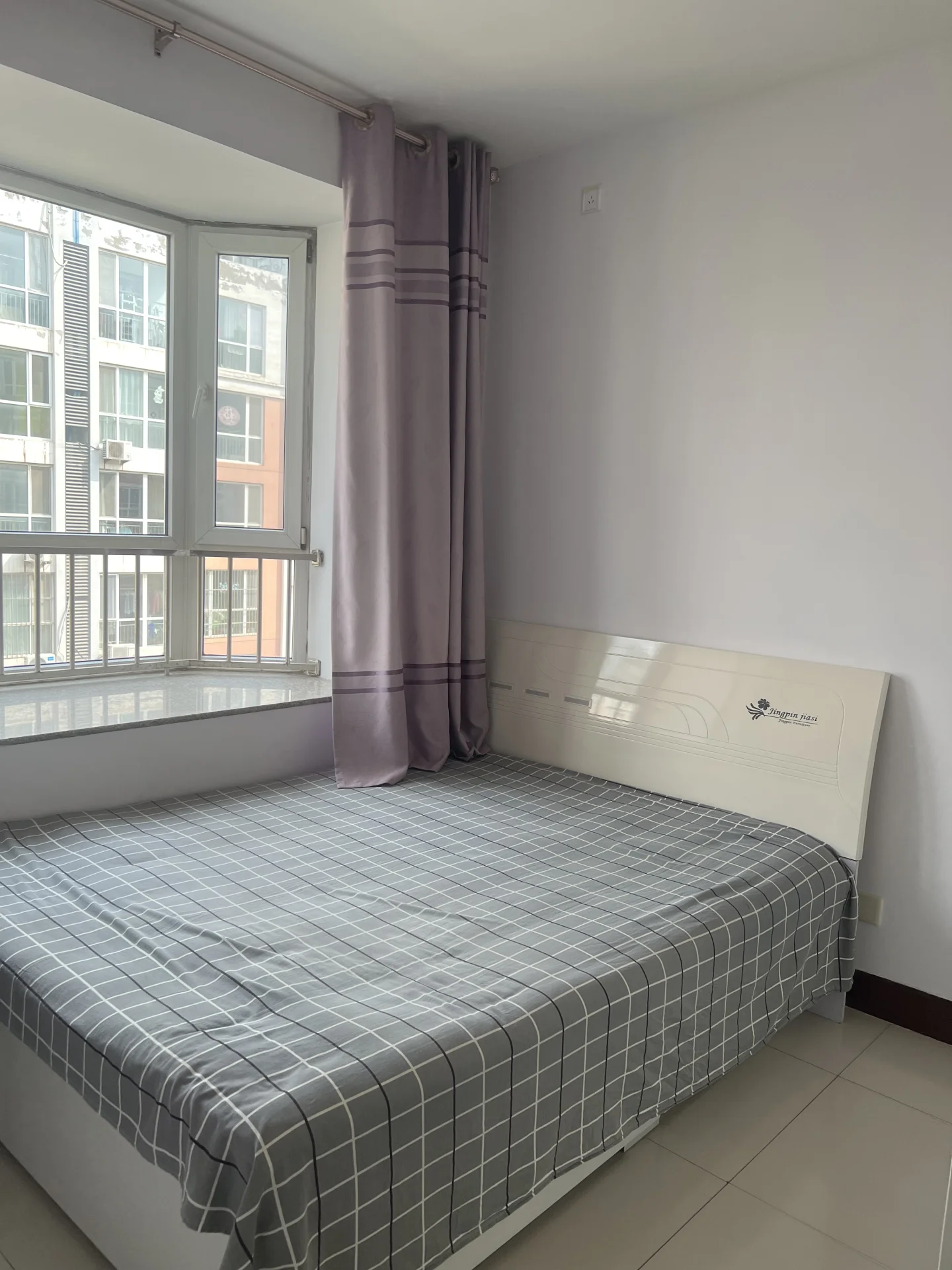 小而温馨的卧室，配有白色床铺和窗户，窗外是城市景色。紫色墙面增添色彩，电视提供娱乐。整体氛围宁静宜人，是放松或休息的理想之地。关键字:卧室 白色床铺 窗户 城市景色 紫色墙面 电视