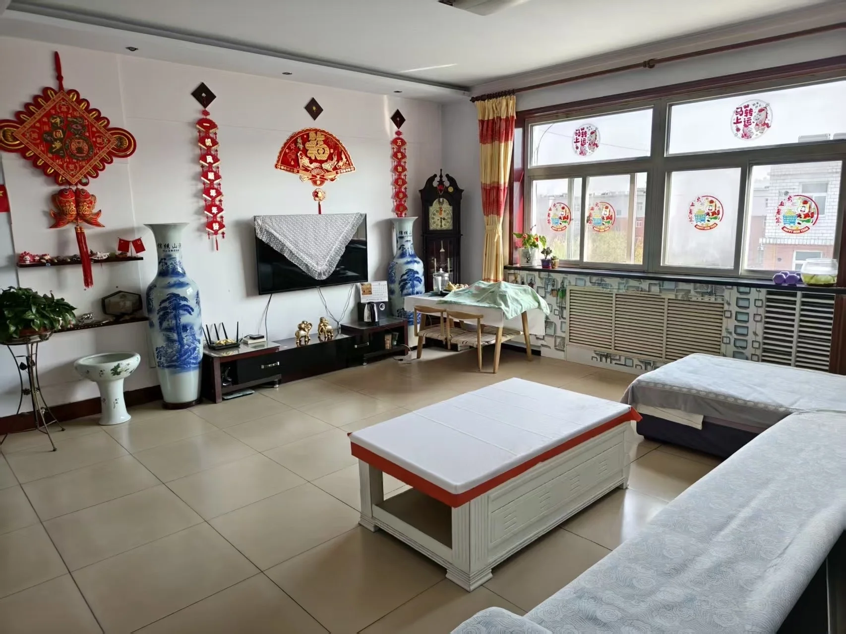 宽敞明亮的客厅，白色瓷砖地面和墙面，电视墙饰点缀，沙发、长椅和餐桌椅布局合理，大窗户采光充足。关键字:客厅 白色瓷砖 电视墙饰 沙发 长椅 餐桌椅 大窗户