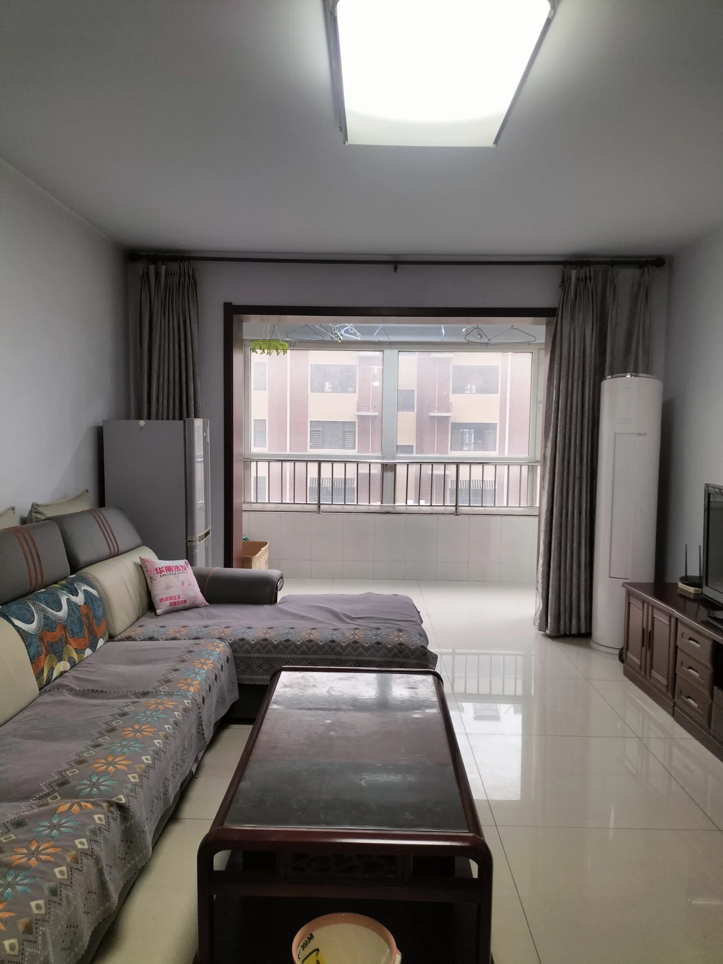 宽敞明亮的客厅，白色墙面，沙发、咖啡桌、电视一应俱全。背景有窗户，自然光洒进室内。两张床中一张有枕头，营造出宁静舒适的氛围，家具布局合理，装饰温馨宜人。关键字:客厅 白色墙面 沙发 咖啡桌 电视 窗户 自然光 床 枕头