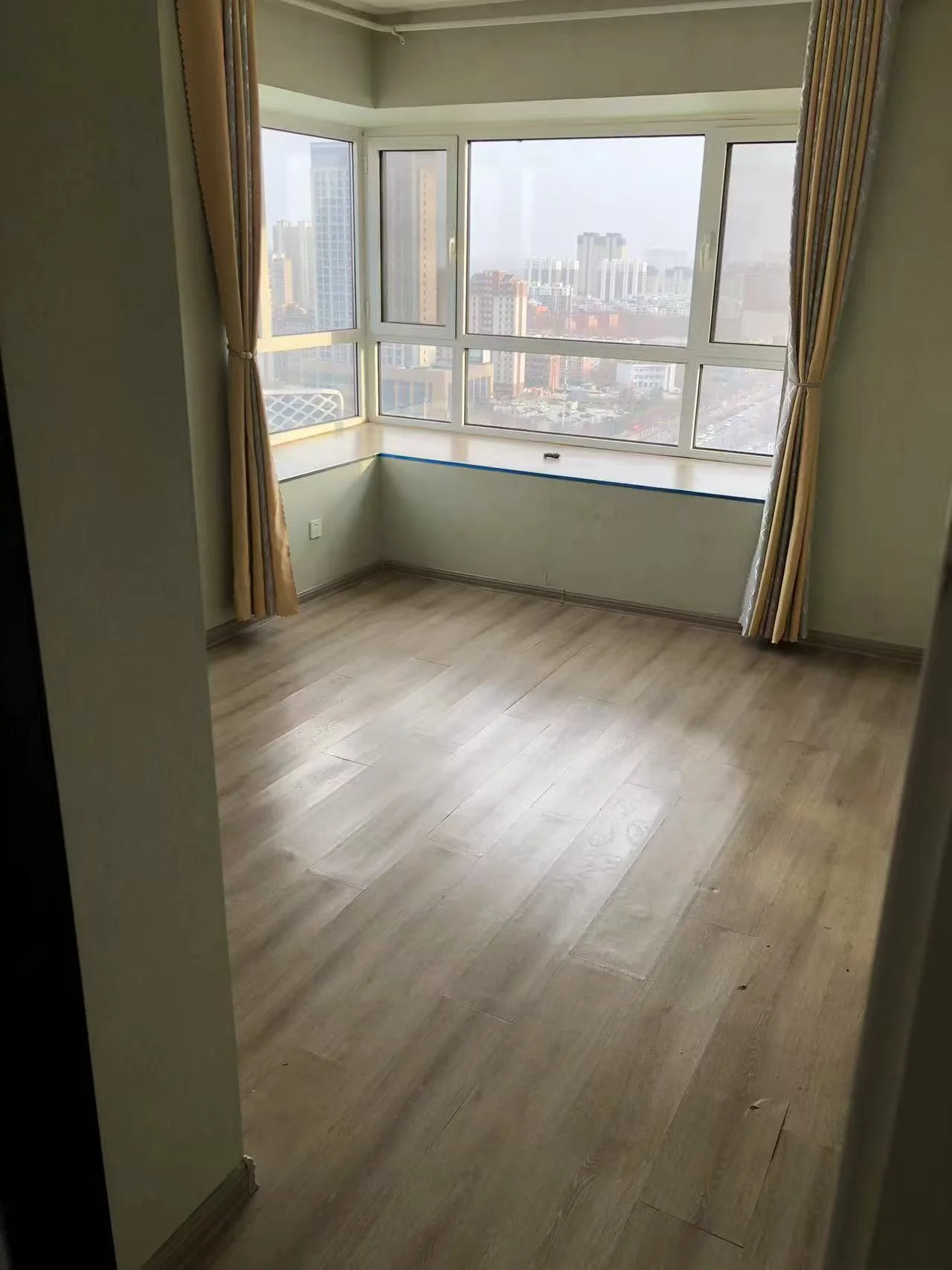 宽敞明亮的房间，白墙木质地板，窗外城市景色。现代简约风格，线条流畅，装饰简洁。宁静宜人，仿佛城市喧嚣的避风港。关键字:宽敞 明亮 白墙 木质地板 城市景色 现代简约 宁静宜人