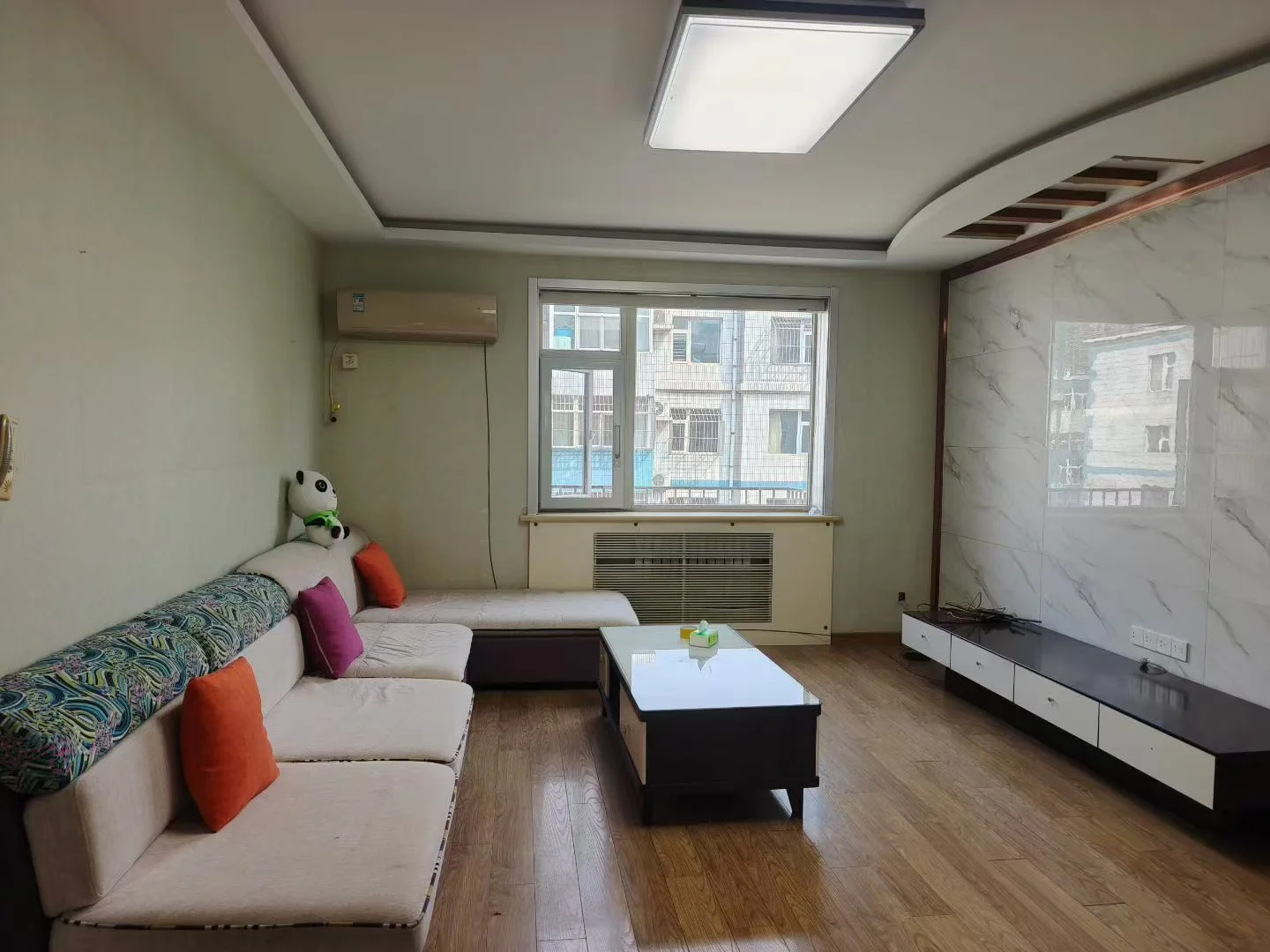 宽敞明亮的客厅，白色墙面和木质地板，沙发、椅子和咖啡桌营造温馨氛围，窗外建筑景观增添空间感。关键字:大客厅 白色墙面 木质地板 沙发 椅子 咖啡桌 窗户景观