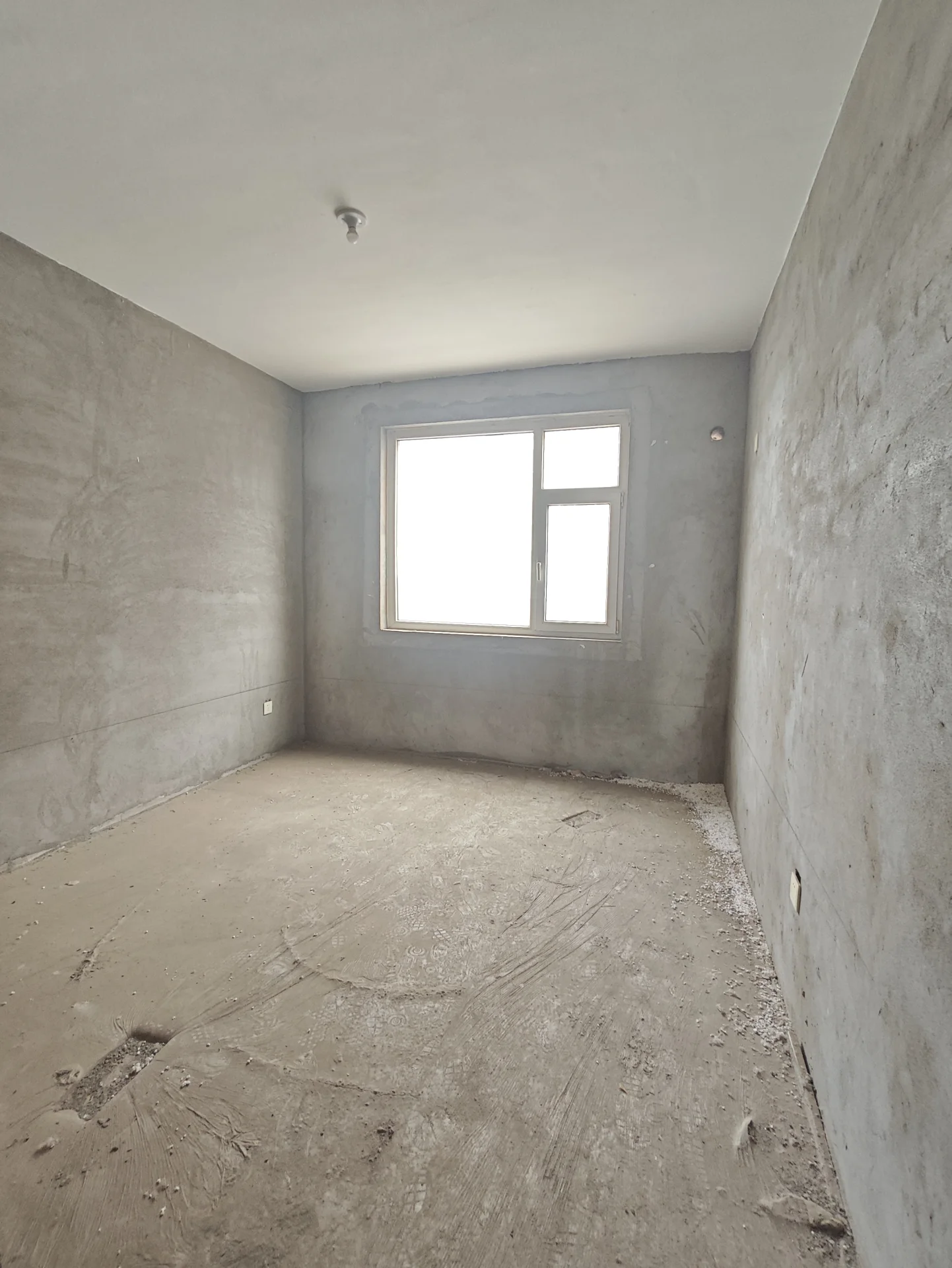 宽敞明亮的房间，混凝土墙面和地板，自然光透过窗户洒进，营造出宁静和谐的氛围。房间显得正在装修或刚刚翻新，透露出未完成的质感。家具和装饰的缺失进一步强调了空间的空旷与简约。关键字:宽敞 明亮 混凝土 自然光 宁静 装修 简约