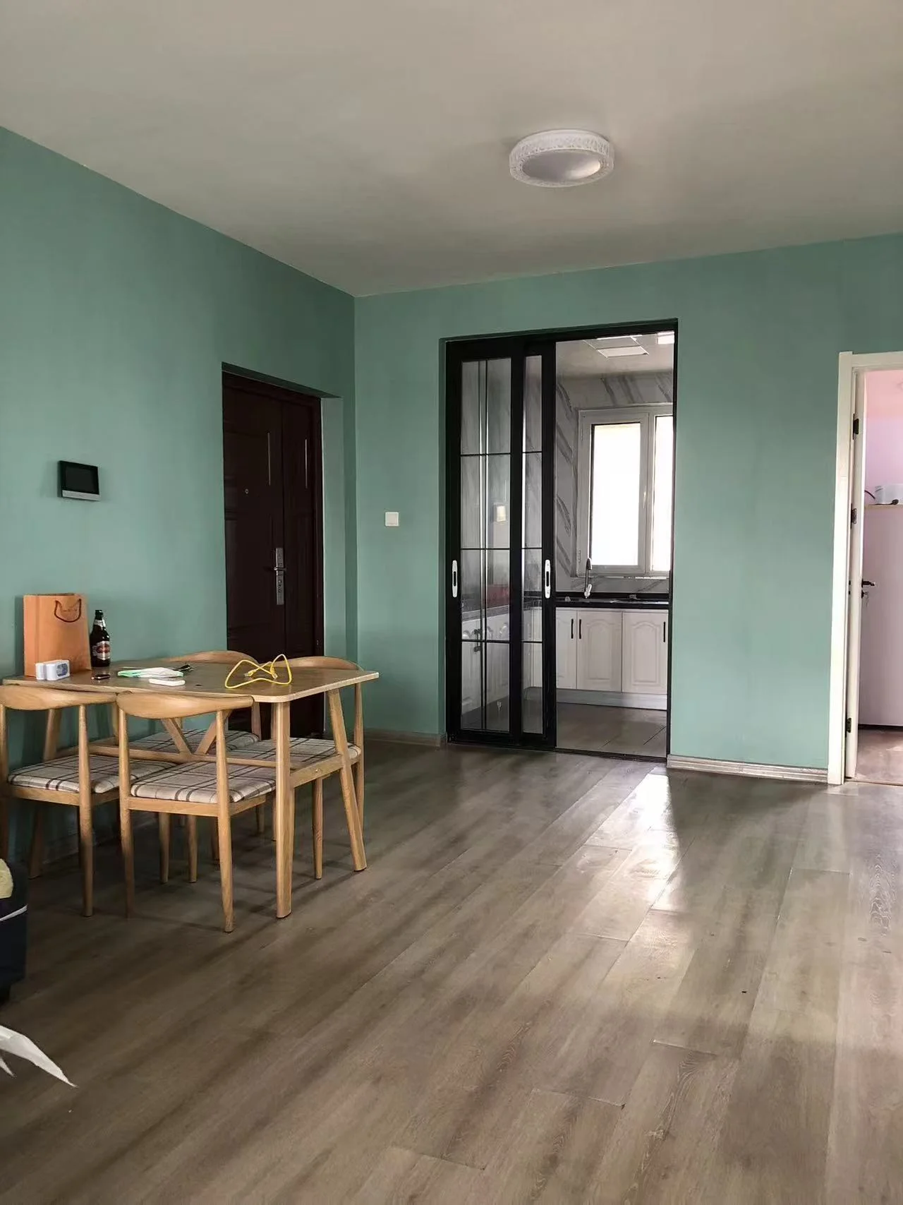 宽敞明亮的客厅，硬木地板，中心摆放着餐桌和椅子，旁边是配备水槽和烤箱的厨房。蓝色调的墙面增添了几分优雅，室内的装饰品如瓶子、杯子、碗和花瓶点缀其间，一盆绿植为空间增添了生机。关键字:客厅 硬木地板 餐桌 椅子 厨房 水槽 烤箱 蓝色调 装饰品 绿植