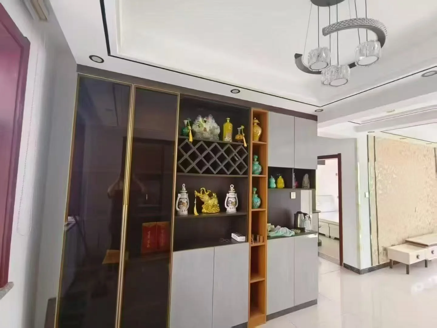 宽敞明亮的厨房，白色橱柜与黑色台面形成鲜明对比，墙上酒架上摆满了葡萄酒，上方装饰着两尊花瓶，厨房内散落几只杯子，整体氛围温馨有序。关键字:大厨房 白色橱柜 黑色台面 酒架 葡萄酒 花瓶 杯子