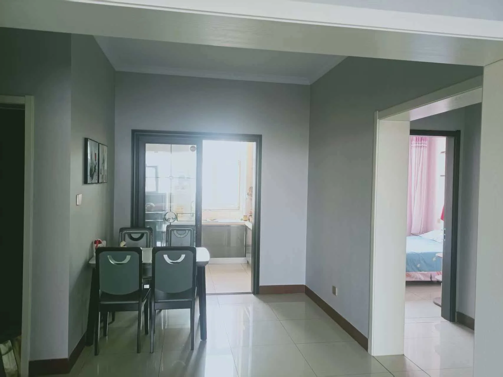 这是一间干净整洁的客厅，白色瓷砖地面，营造出宁静而优雅的氛围。沙发、椅子、餐桌和冰箱等家具家电摆放有序。两盆植物和两个花瓶增添了几分生机。整体空间舒适宜人。关键字:客厅 白色瓷砖 沙发 椅子 餐桌 冰箱 植物 花瓶 宁静氛围