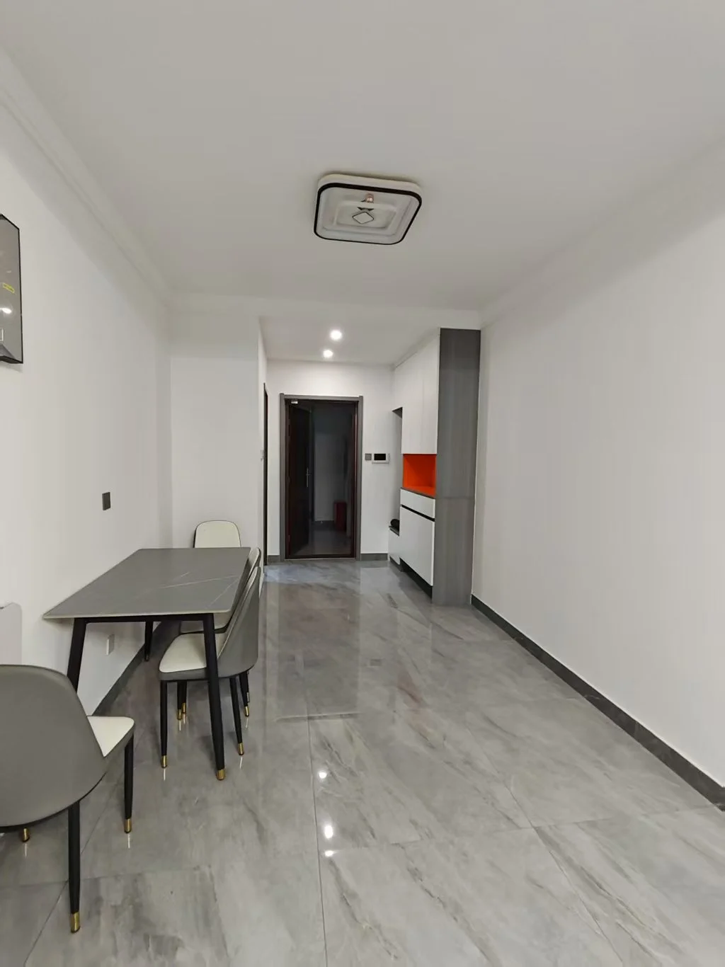 宽敞明亮的房间，白色墙面，灰色地板，大窗户采光良好。中央摆放着一张餐桌和四把椅子，背景有冰箱，可能是厨房或餐厅。空旷无杂物，营造出宁静简约的氛围。关键字:白色墙面 灰色地板 大窗户 餐桌 椅子 冰箱 厨房 餐厅 宁静简约