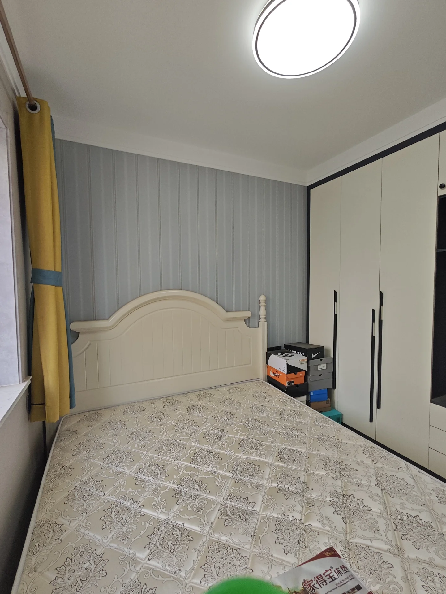 卧室布置整洁，床位于角落，上方吊灯提供充足光线。白色墙壁营造宁静氛围，整体简约舒适，无杂物。关键字:卧室 整洁 床 吊灯 白色墙壁 宁静氛围