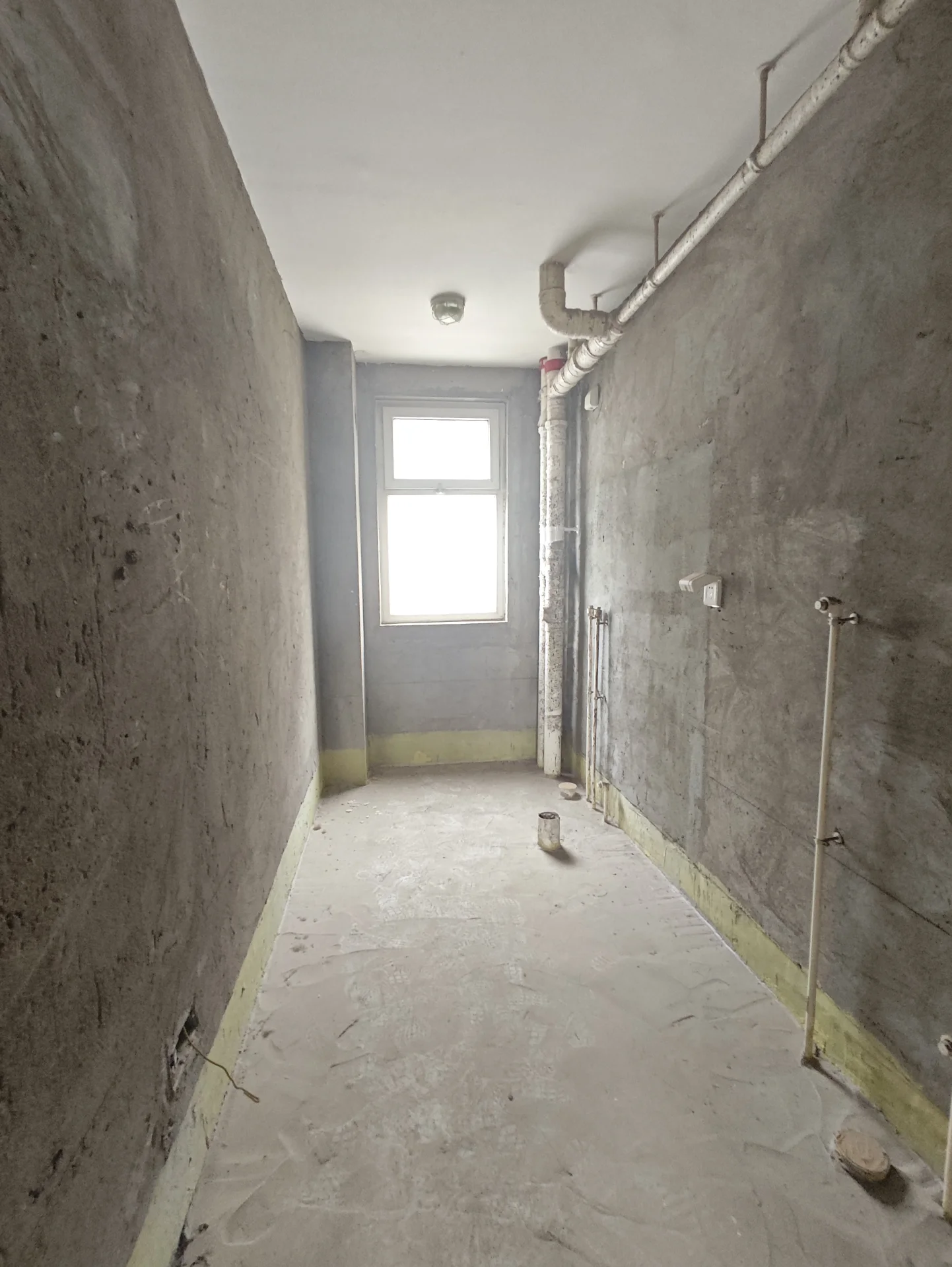 宽敞的房间，水泥墙面和地板，显得正在施工或翻新。一只猫安静地坐在中央，仿佛对周围环境无动于衷。角落有一扇窗户，自然光洒进来。整个空间显得宁静而略带诡异，因为没有家具或人。关键字:宽敞 水泥墙面 施工 翻新 猫 自然光 宁静 诡异