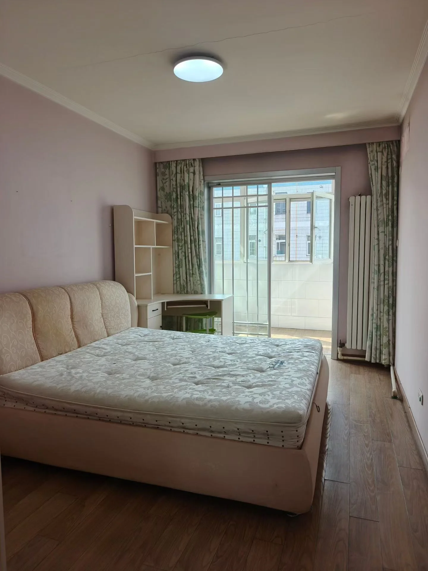 温馨舒适的卧室，大床居中，沙发靠墙，窗户采光自然。书桌椅方便工作学习。粉色墙壁增添温暖，台灯营造 cozy 氛围，开窗通风使环境更加放松。关键字:卧室 大床 沙发 窗户 自然光 书桌椅 粉色墙壁 台灯 通风