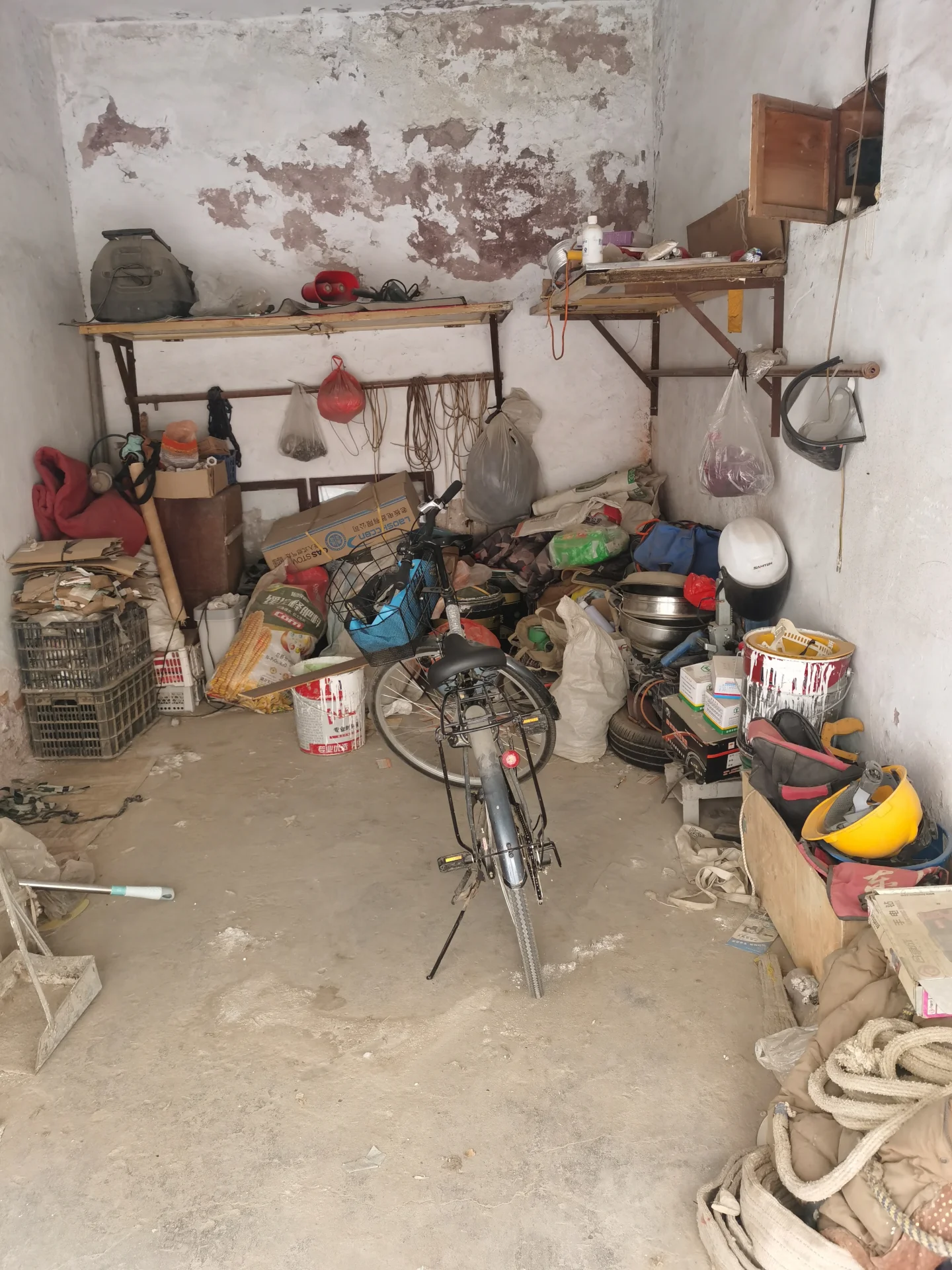 小而杂乱的空间，摆满了各种物品和装饰。房间内有两辆自行车，其中一辆带篮子。还有一辆摩托车。运动球散落在各处。靠近左侧的椅子可见。墙壁上满是书架和物品，显得有些杂乱。关键字:小空间 杂乱 自行车 摩托车 运动球 椅子 书架