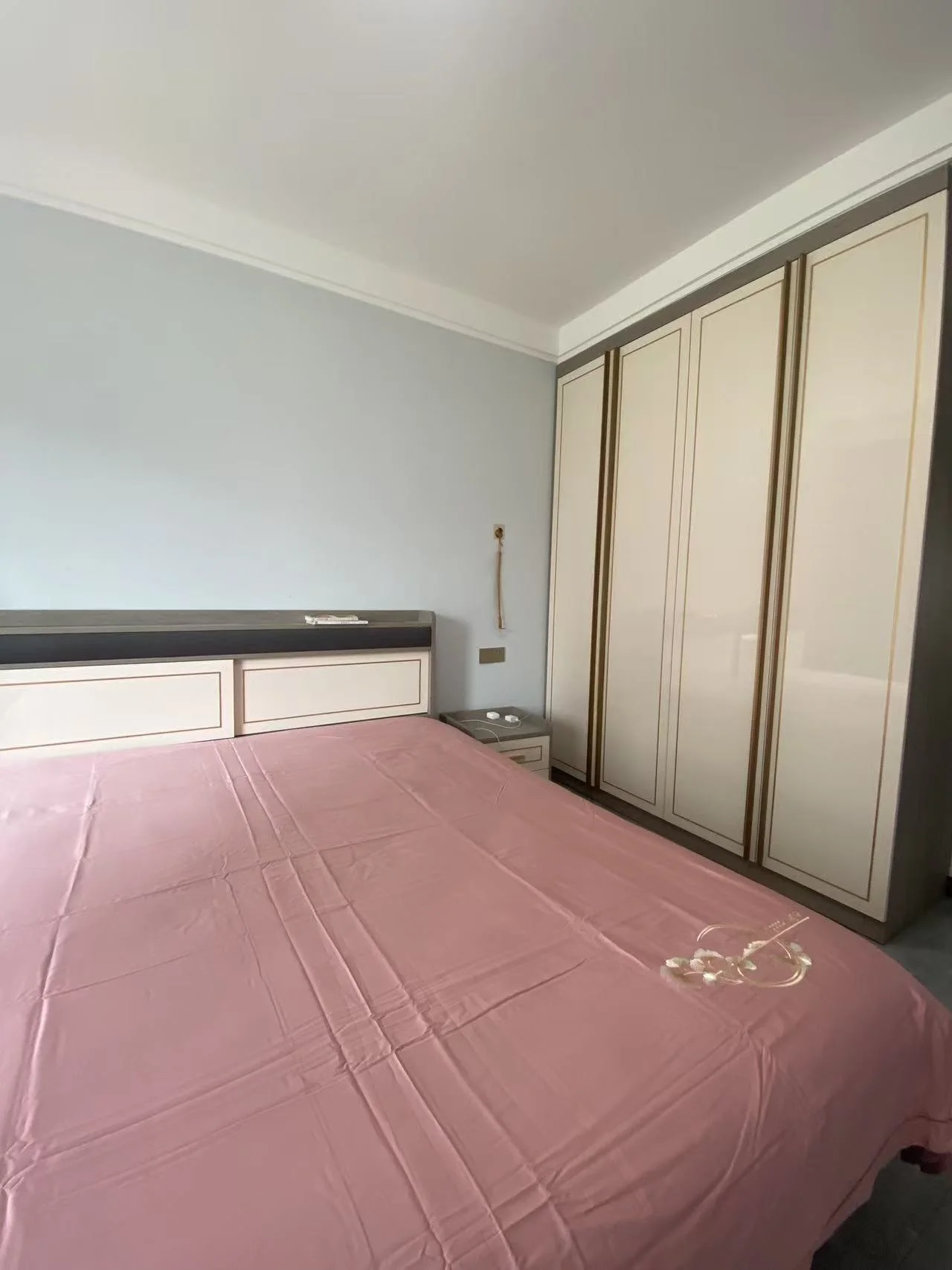 卧室宽敞，粉色床单舒适，衣柜和梳妆台整洁有序。床头三架书架装饰雅致，桌椅齐全的工作区增添实用感。整体氛围宁静宜人，是放松或休息的理想选择。关键字:卧室 粉色床单 衣柜 梳妆台 书架 工作区 宁静