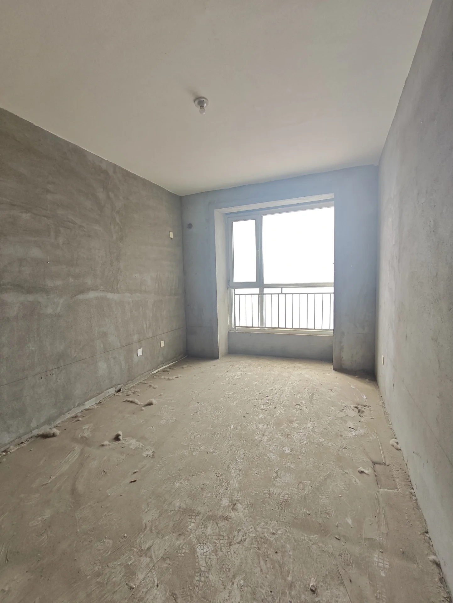 宽敞的空房间，水泥墙面和地板，一扇窗户引入自然光。空间显得在施工或未完成状态，没有家具或装饰。氛围宁静而安静，没有活动迹象。简约风格的建筑线条简洁，整体给人以空旷、未被占用的感觉。关键字:宽敞 空房间 水泥墙面 自然光 施工中 未完成 简约风格 宁静氛围