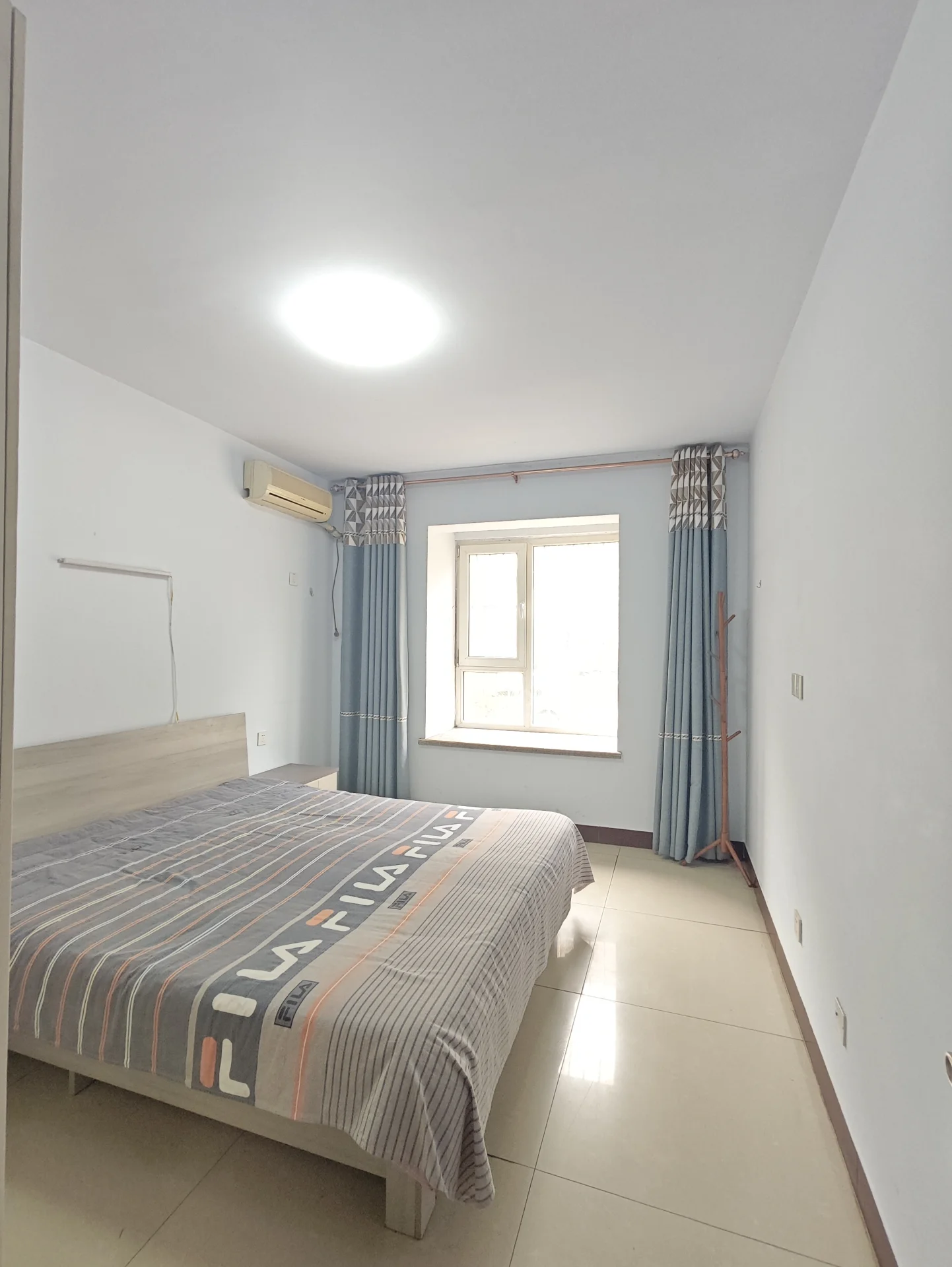 小而整洁的卧室，白色墙壁，大窗户采光充足，床占据主要空间，氛围宁静简约。关键字:小卧室 白色墙壁 大窗户 自然光 床 宁静氛围 简约设计