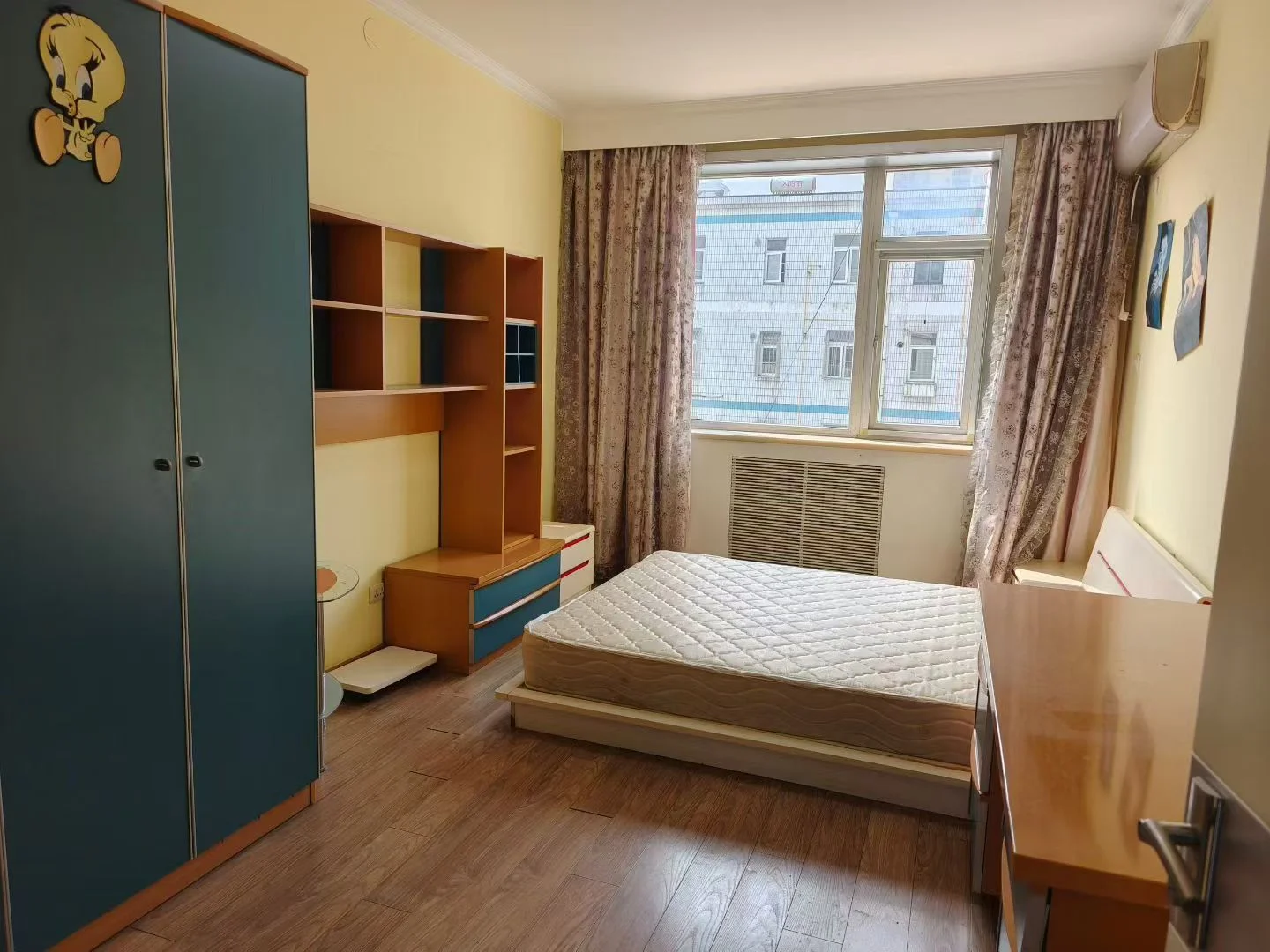 温馨舒适的卧室，木质地板，黄色墙壁，蓝色衣柜，窗户透光，床铺在地面上，两侧各有两把夜柜。简约实用的风格，没有复杂装饰，营造出宁静和平和的氛围。关键字:卧室 木质地板 黄色墙壁 蓝色衣柜 窗户 床铺 夜柜 简约风格 宁静氛围