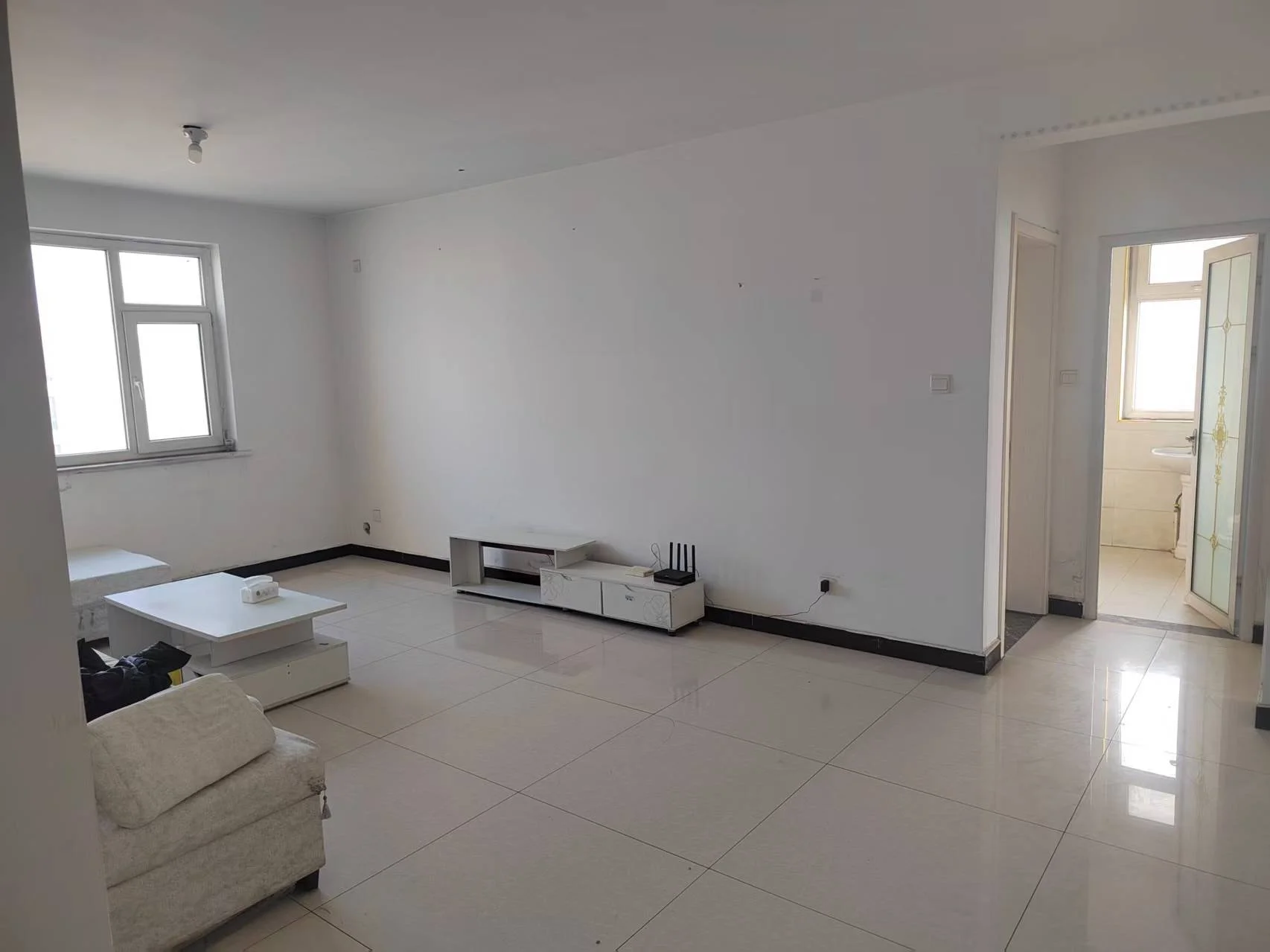 宽敞明亮的客厅，白色墙面和地板，两侧各有一张沙发，中央摆放一张餐桌，整体干净整洁，充满休闲娱乐氛围。关键字:宽敞 明亮 白色墙面 沙发 餐桌 干净整洁 休闲娱乐