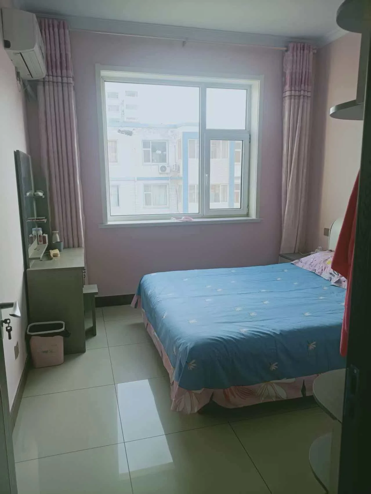 小卧室，蓝色床，窗户，镜子。阳光透过窗户洒进房间，粉色墙壁营造温馨氛围。衣柜增添实用性，整体风格简洁干净。关键字:小卧室 蓝色床 窗户 镜子 阳光 粉色墙壁 温馨氛围 衣柜 简洁干净