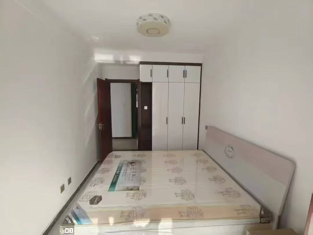 小卧室，白色床置于角落，木制头板，两侧有夜stands。房间整洁有序，背景有门通向其他空间。整体氛围宁静祥和，适合休息放松。关键字:小卧室 白色床 木制头板 夜stands 整洁有序 宁静祥和