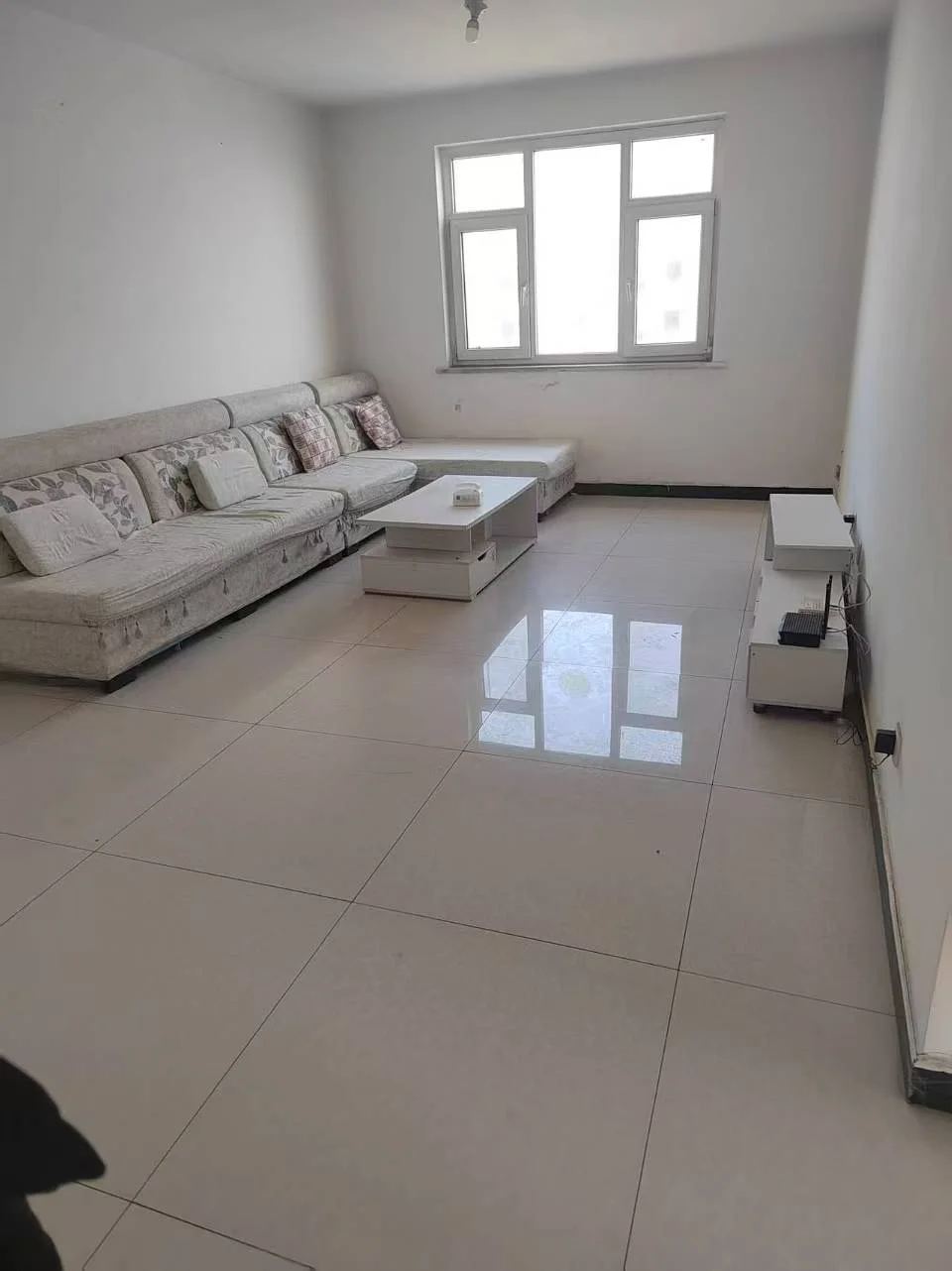 宽敞明亮的客厅，白色墙壁，瓷砖地面，大窗户。沙发靠墙摆放，两把椅子在前方，咖啡桌中央，营造舒适的休息和交流空间。目前为空间显得宁静祥和。大窗户引入自然光，营造明亮欢迎的氛围。整体简约而温馨，注重功能与舒适。关键字:宽敞 明亮 白色墙壁 瓷砖地面 大窗户 沙发 椅子 咖啡桌 宁静祥和 自然光