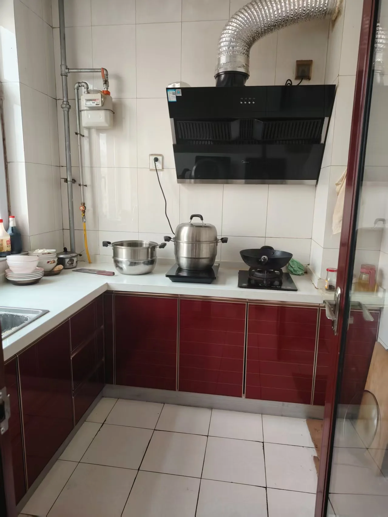 小厨房内，黑色灶台与上方通风口相得益彰，白色台面整洁有序，大中小锅错落有致，营造出宁静舒适的氛围。关键字:小厨房 黑色灶台 通风口 白色台面 大中小锅 宁静舒适