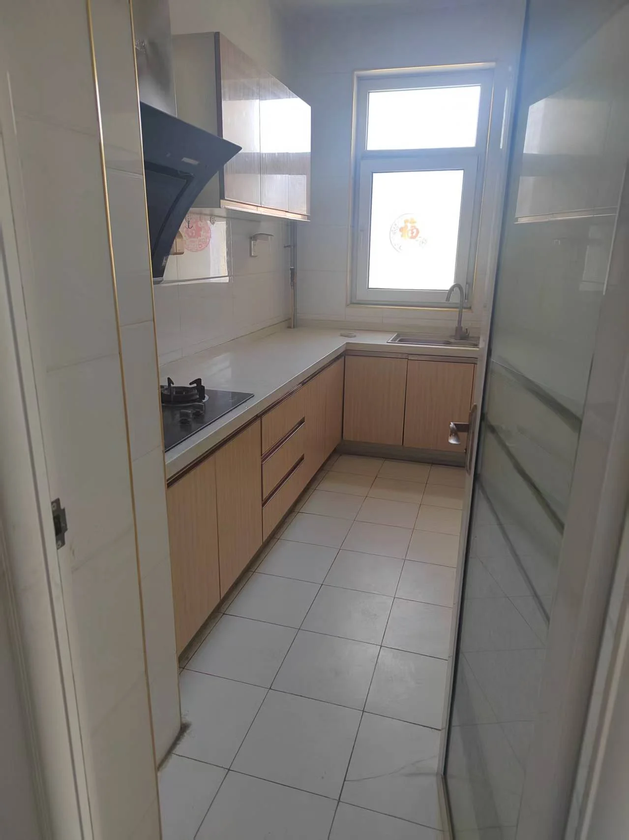 厨房小巧明亮，白色瓷砖地面，木质橱柜整洁。配备洗碗机、灶台、微波炉和冰箱。两侧各有一扇窗户，阳光透过窗户营造出温馨舒适的氛围。关键字:小厨房 白色瓷砖 木质橱柜 洗碗机 灶台 微波炉 冰箱 窗户 阳光