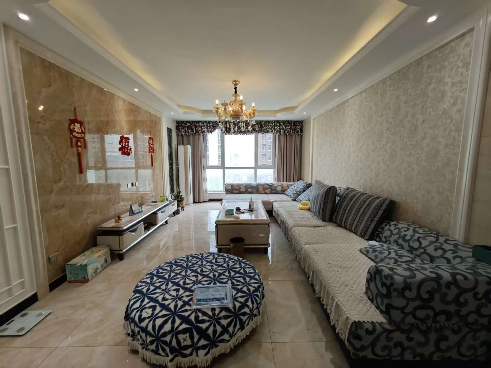 宽敞明亮的客厅，配有大沙发、两把椅子和咖啡桌，墙上和家具上点缀着蓝色和白色的装饰，营造出优雅而精致的氛围。电视挂在墙上，提供娱乐。书籍散落其间，增添温馨气息。客厅流畅地过渡到餐厅，有餐桌和椅子。大窗户让自然光充满房间，明亮开阔。整体环境宜人舒适，适合放松或招待客人。关键字:宽敞客厅 优雅装饰 自然光 大沙发 电视 书籍