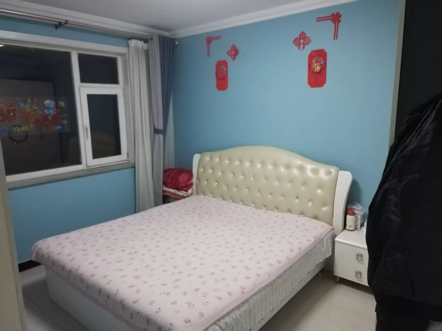 卧室中央摆放着一张白色床，粉色床单增添温馨氛围，窗户采光自然，墙上两支红色消防栓别具一格，窗边有一把椅子增加舒适度。关键字:卧室 白色床 粉色床单 自然采光 红色消防栓 椅子