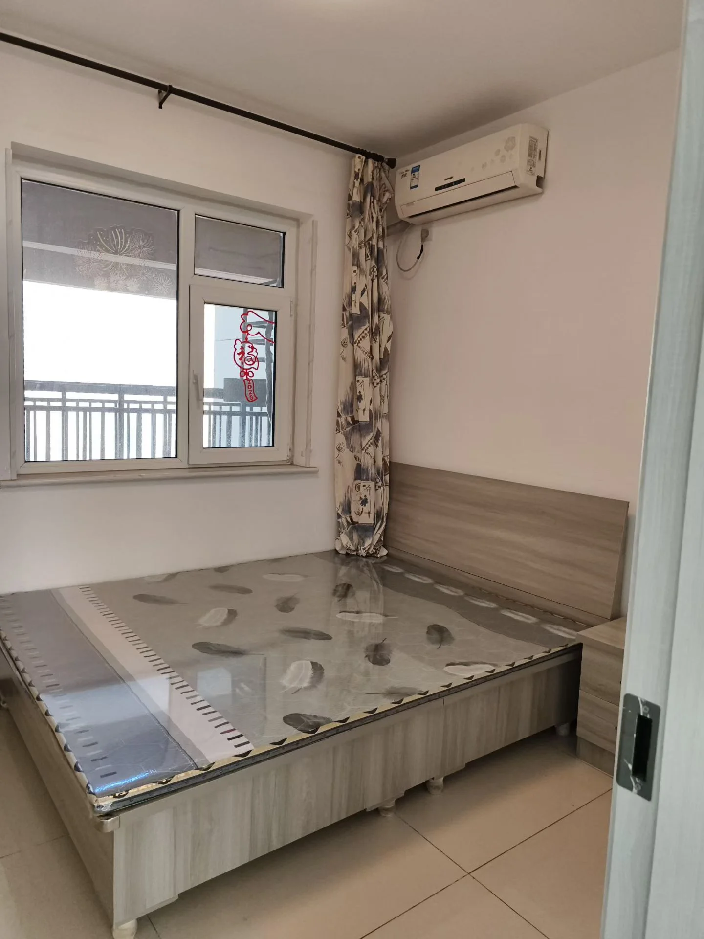 小卧室，白色墙壁，一扇窗户。角落摆放着一张大床，配有玻璃顶。床上方有空调单元。房间整洁干净，氛围宁静平和，目前为空闲状态。关键字:小卧室 白色墙壁 窗户 大床 玻璃顶 空调单元 整洁干净 宁静平和