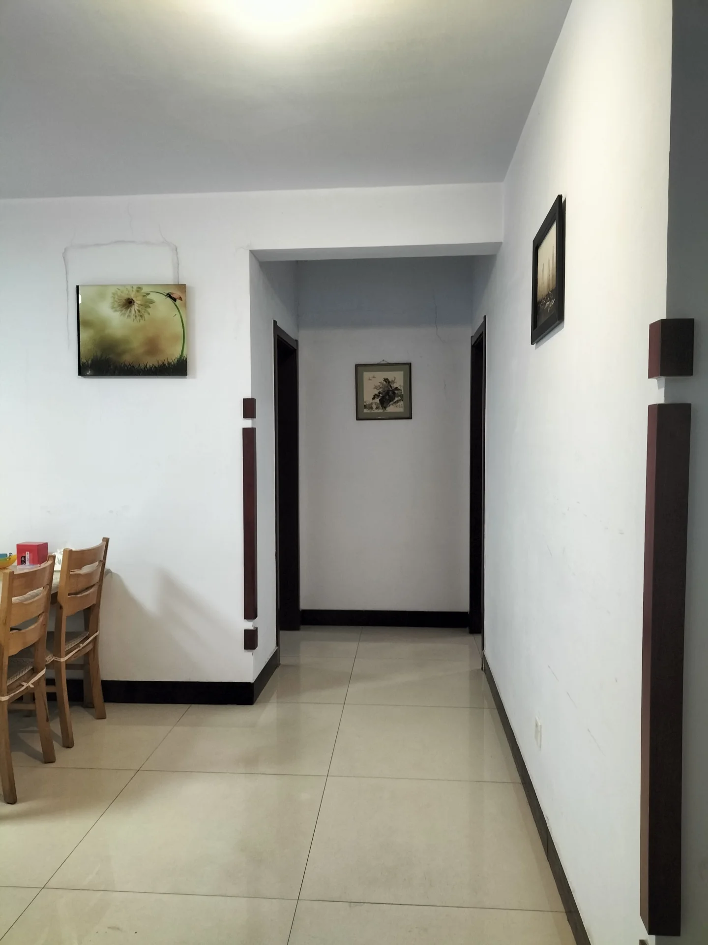 空置餐厅的走廊，白色墙壁和瓷砖地面，墙上挂着一幅猫的画，尽头有通向另一房间的门，氛围宁静优雅。关键字:餐厅 走廊 白色墙壁 瓷砖地面 猫的画 宁静优雅