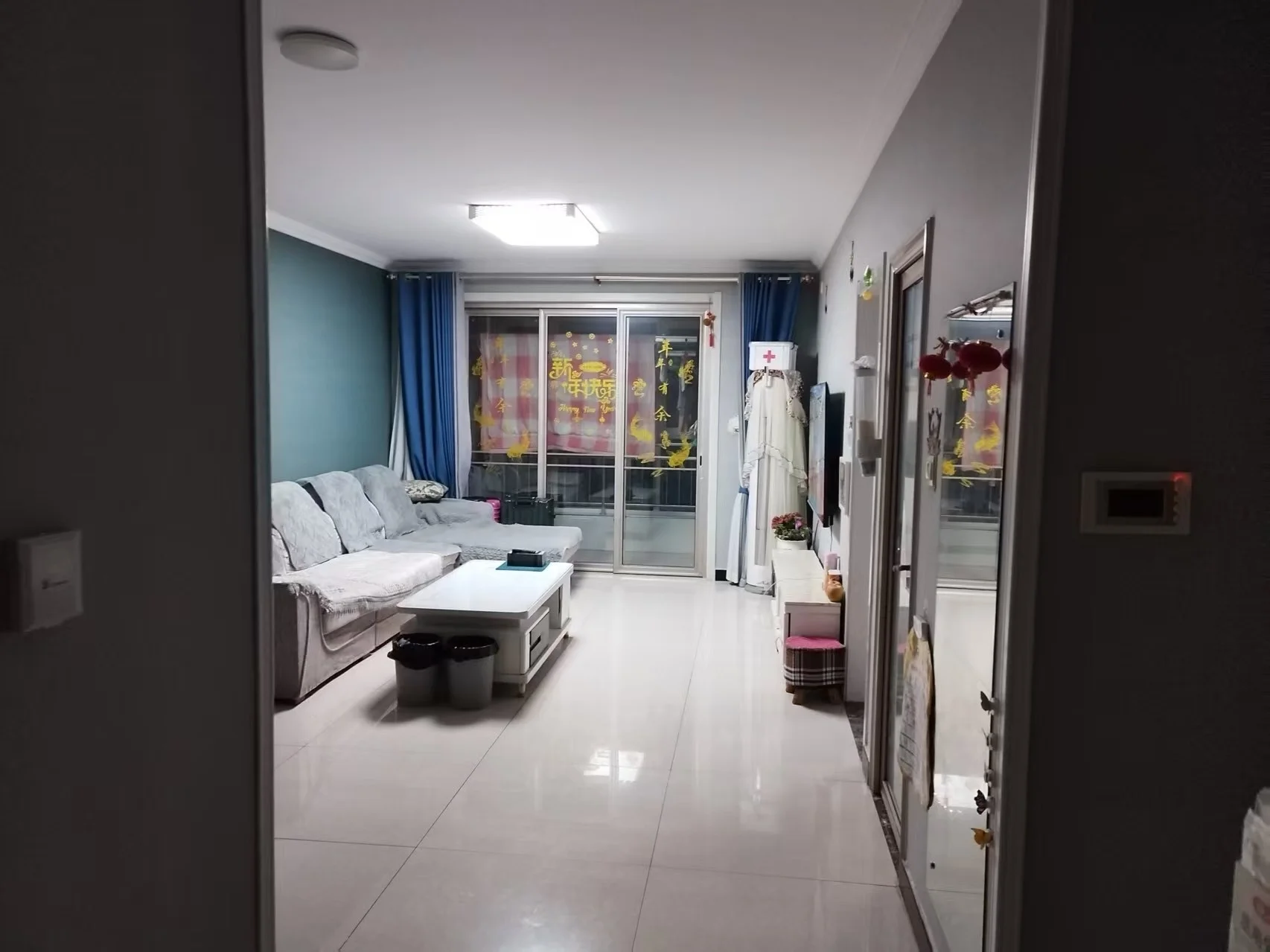 宽敞明亮的客厅，白色瓷砖地面和墙壁，中央摆放着沙发，周围是椅子、桌子和柜子。书籍散落在空间中，营造温馨氛围。大窗户引入自然光，营造宁静舒适的环境。关键字:宽敞 明亮 白色瓷砖 沙发 椅子 桌子 柜子 书籍 自然光 宁静舒适