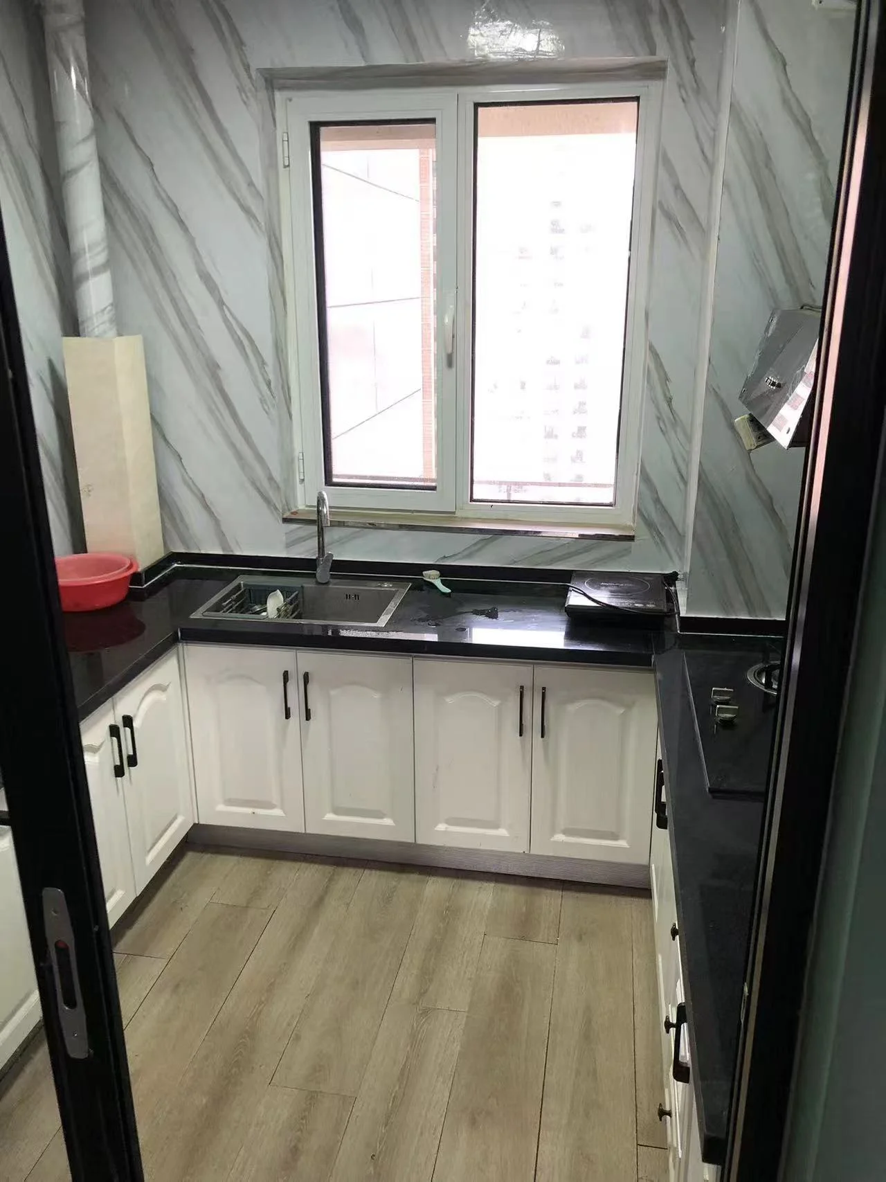 小厨房，黑色台面与白色橱柜搭配，自然光透过窗户洒入，营造出宁静而优雅的氛围。厨房整洁有序，配有洗碗池、烤箱及各种厨具。关键字:小厨房 黑色台面 白色橱柜 自然光 宁静氛围 洗碗池 烤箱 厨具