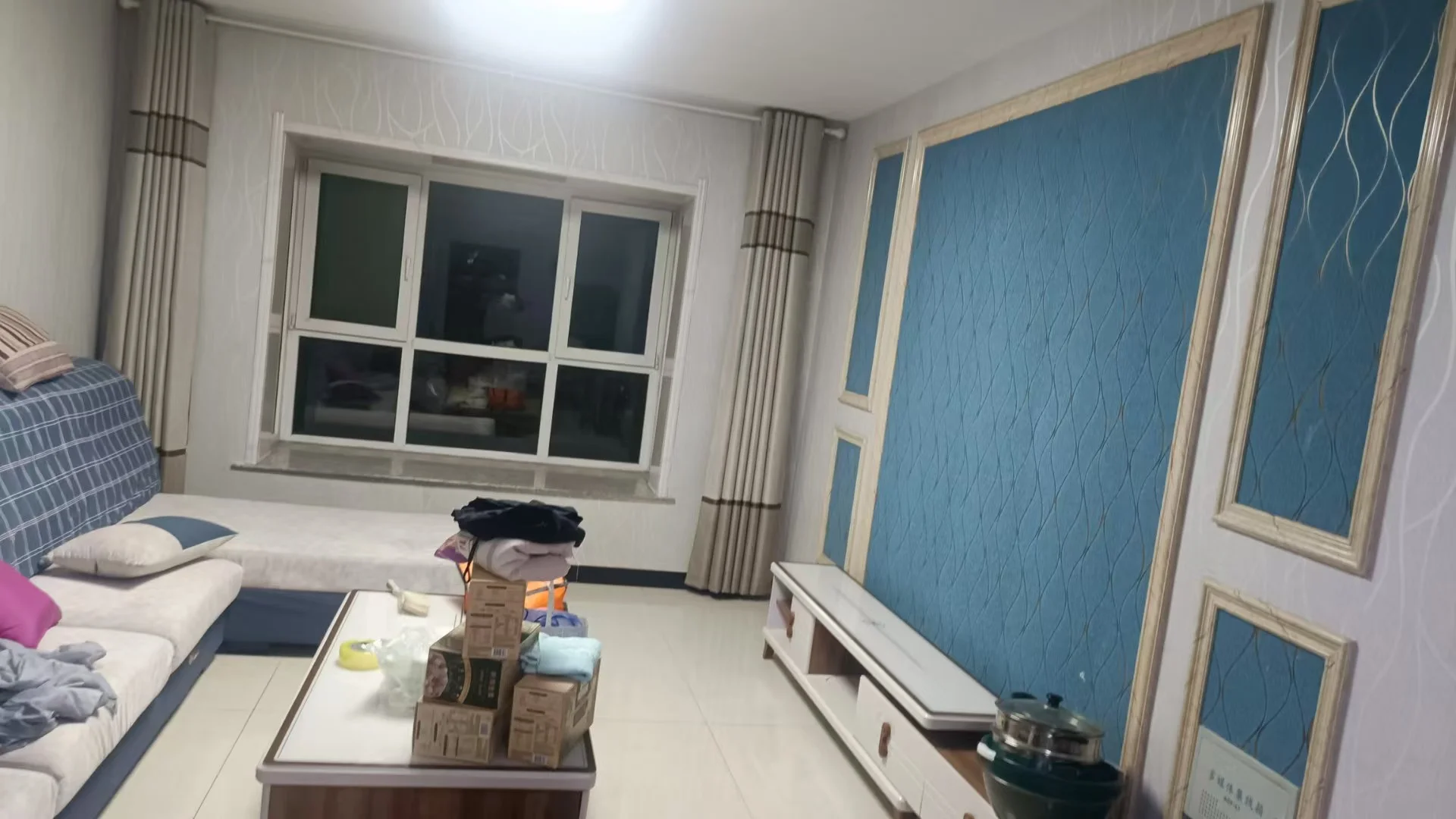 一个宽敞的室内空间，墙面采用蓝色纹理装饰，配有米色沙发和白色窗户。采光良好，整体呈现现代简约的居住氛围。