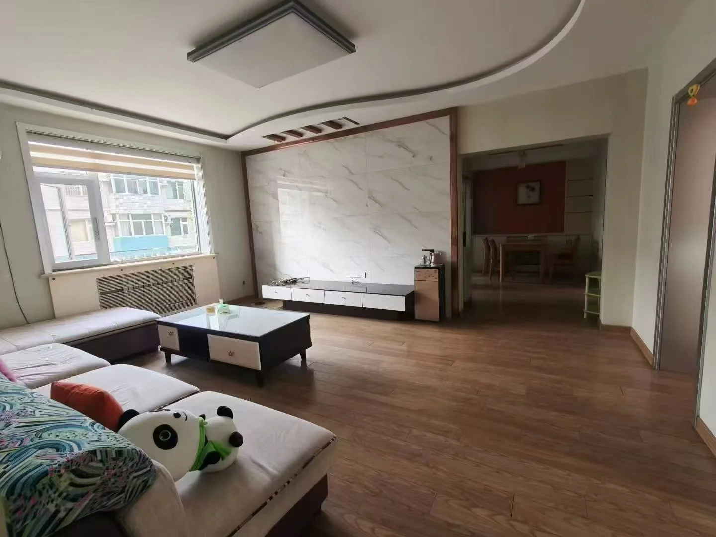 客厅场景，墙面采用大理石纹理，配有简约沙发和电视柜。采光良好，整体呈现现代简约装修风格，氛围整洁舒适。