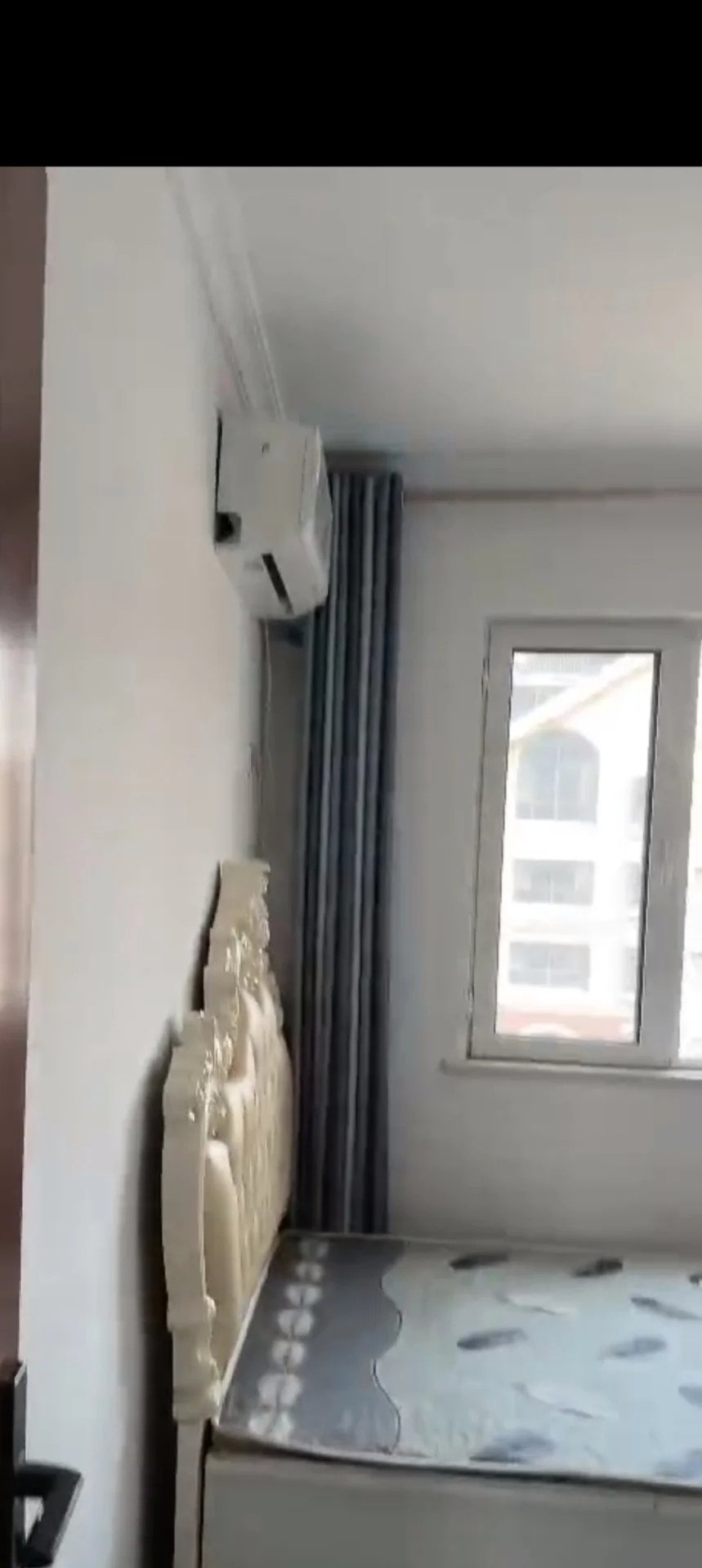 卧室局部场景，墙面为浅色调，配有窗户和空调外机。场景光线明亮，整体呈现简洁、功能性的居住空间氛围。