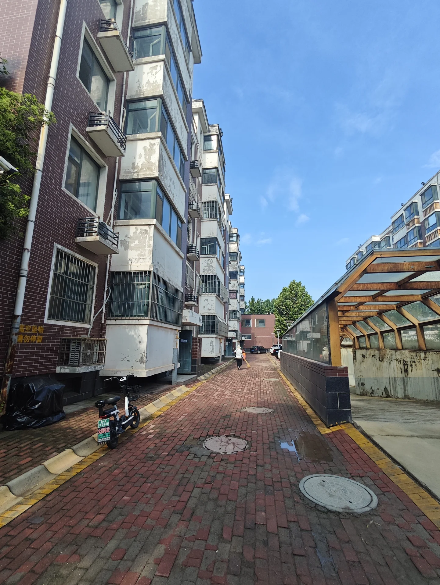 一栋多层现代住宅楼的外部立面，外墙采用红砖和白色装饰相结合的风格。建筑立面有多个窗户和阳台，周围是铺设红砖的街道和一些低矮的建筑，整体呈现典型的城市社区建筑外观，氛围宁静且具有居住属性。