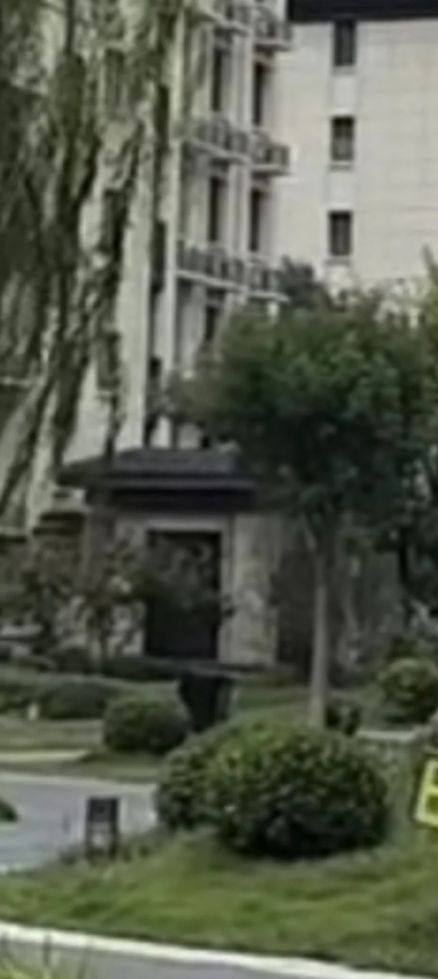 一栋多层建筑的外部立面清晰可见，建筑风格较为传统，外墙呈浅色调，周围有茂密的树木和修剪整齐的草坪，整体环境宁静和谐，具有良好的社区居住氛围。