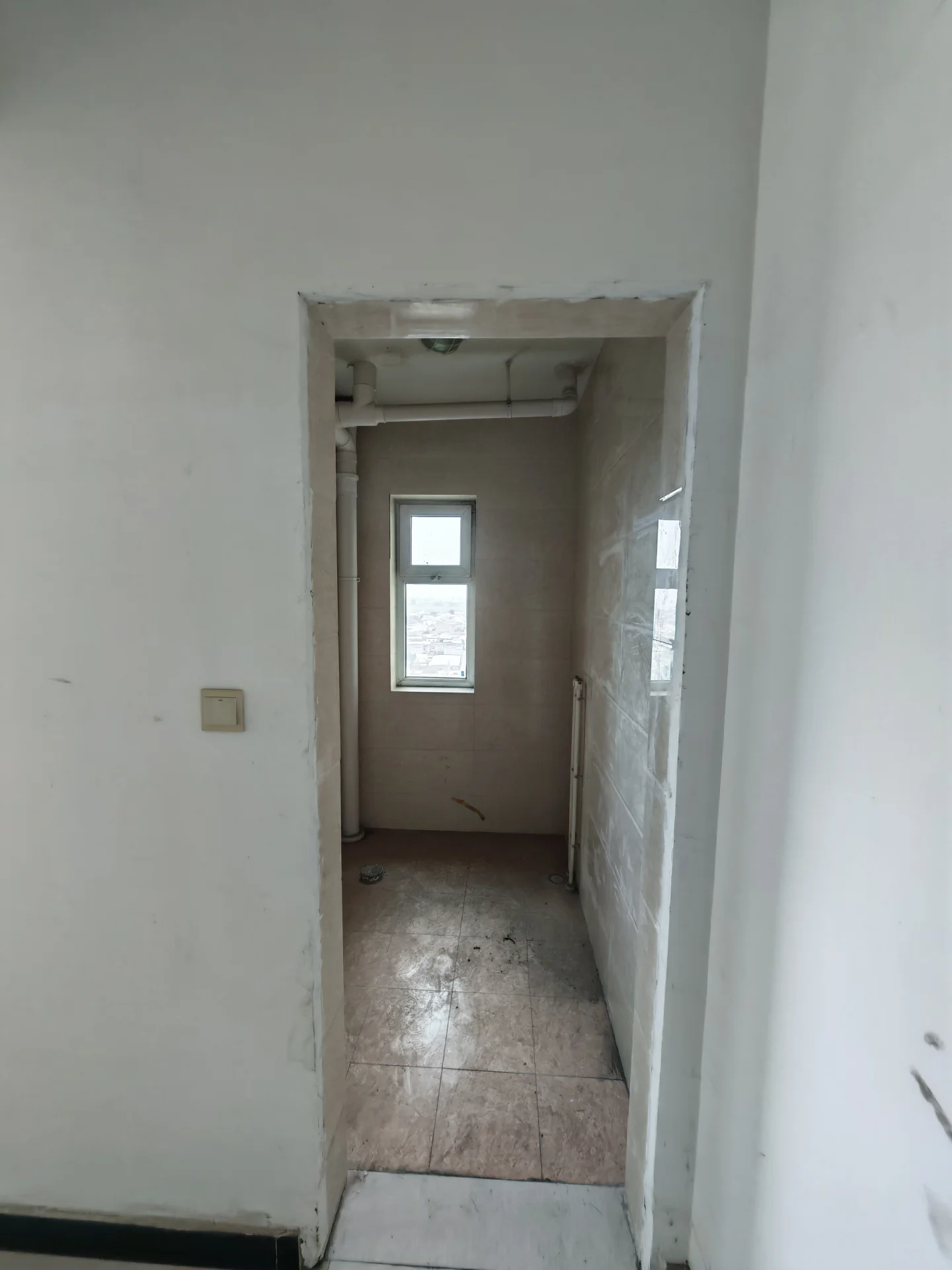 一个室内楼梯空间，墙面为浅色，地面铺设了米色瓷砖，采光有限，整体环境显得较为朴素和空旷。