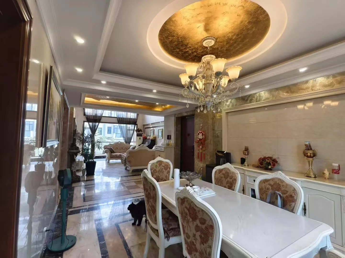 宽敞的用餐区场景，地面铺设木质地板，配有长条形餐桌和带有华丽水晶吊灯。室内装修风格偏向豪华，采光良好，整体氛围大气且温馨。