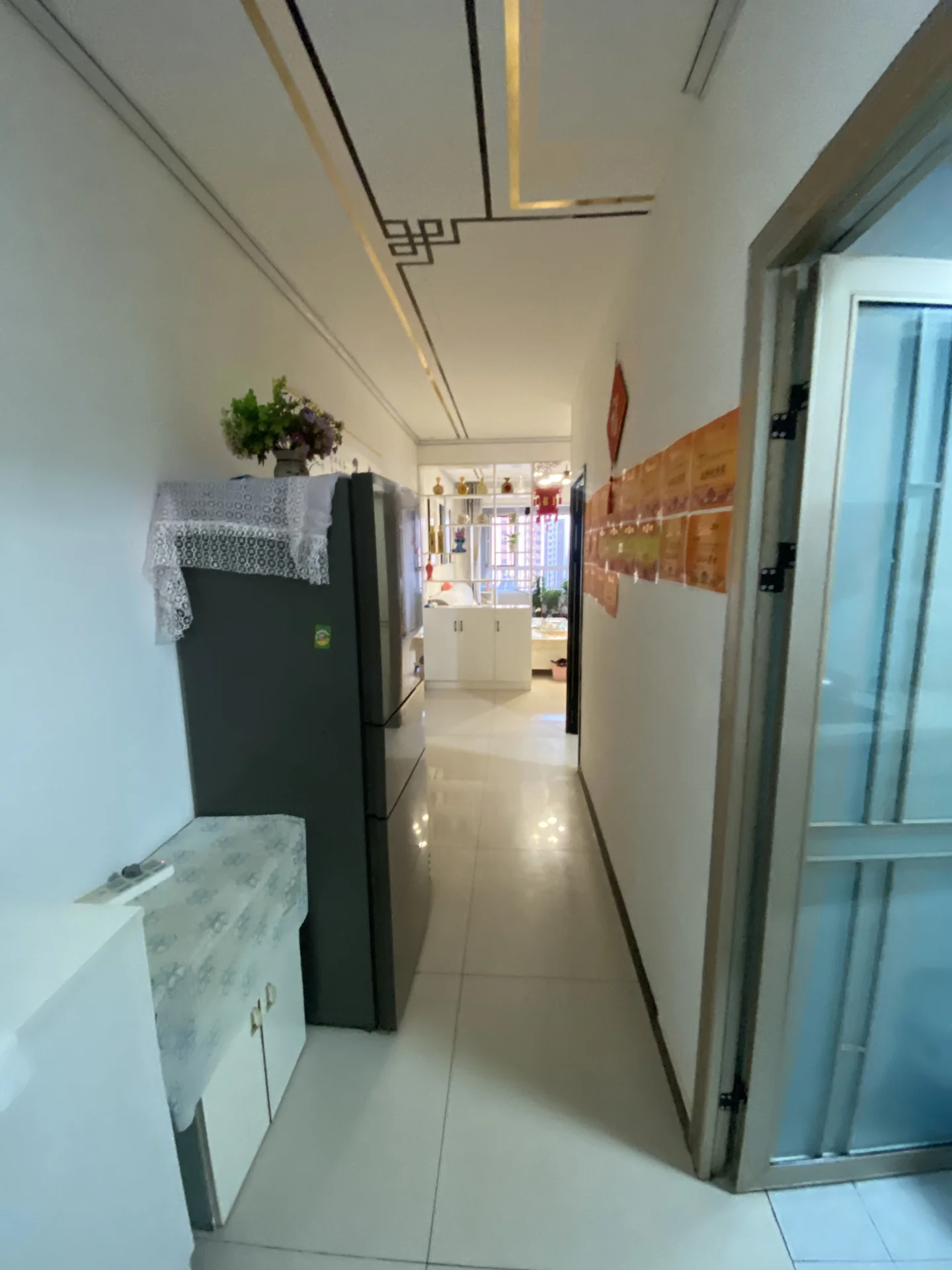 一个现代简约风格的室内空间，地面铺设白色大理石或瓷砖，墙面为白色，天花板上安装了现代风格的线性灯带。空间布局简洁，配有深色储物柜和一些绿植，整体采光良好，呈现出整洁舒适的居住氛围。