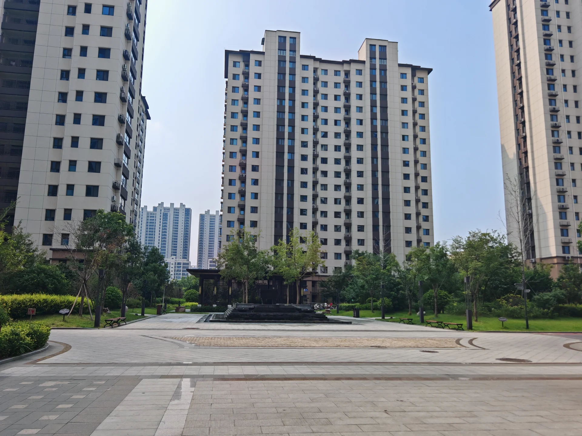 多栋现代风格的高层住宅建筑群，立面以浅色调为主，建筑之间错落有致，前景是精心维护的社区绿化带和中心景观池塘，整体呈现出宁静、现代的城市居住氛围。